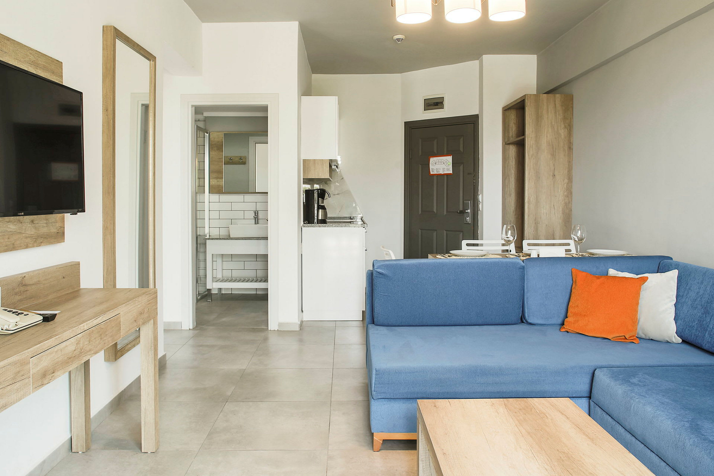 Ett hotellrum med blå soffa, skrivbord, TV, kök och badrum. (AI-genererad text)