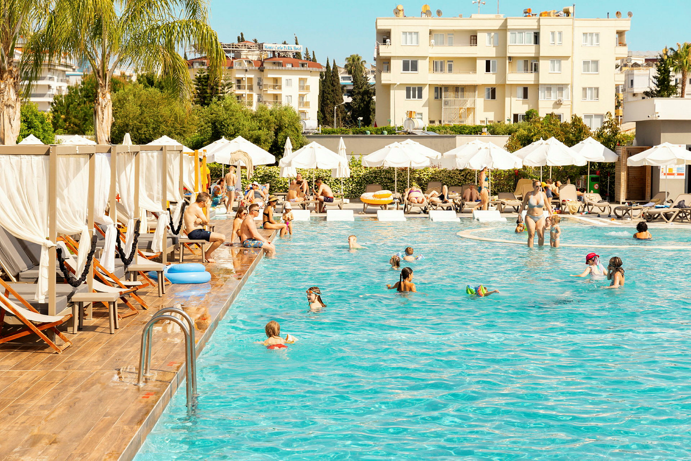 Människor njuter av en pool omgiven av solstolar och parasoller vid ett hotellområde. (AI-genererad text)