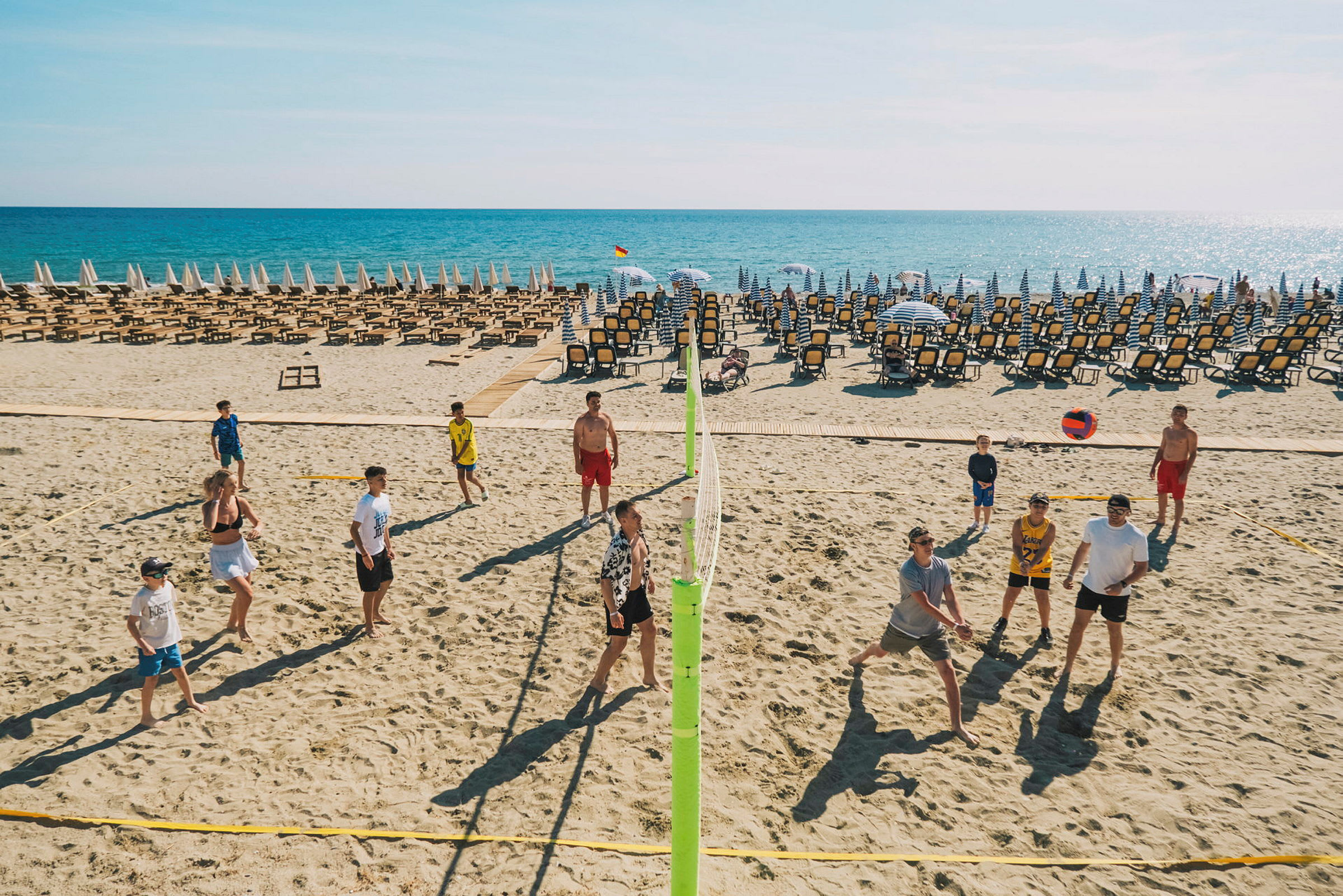 En strand med solstolar och parasoller, människor spelar volleyboll. (AI-genererad text)