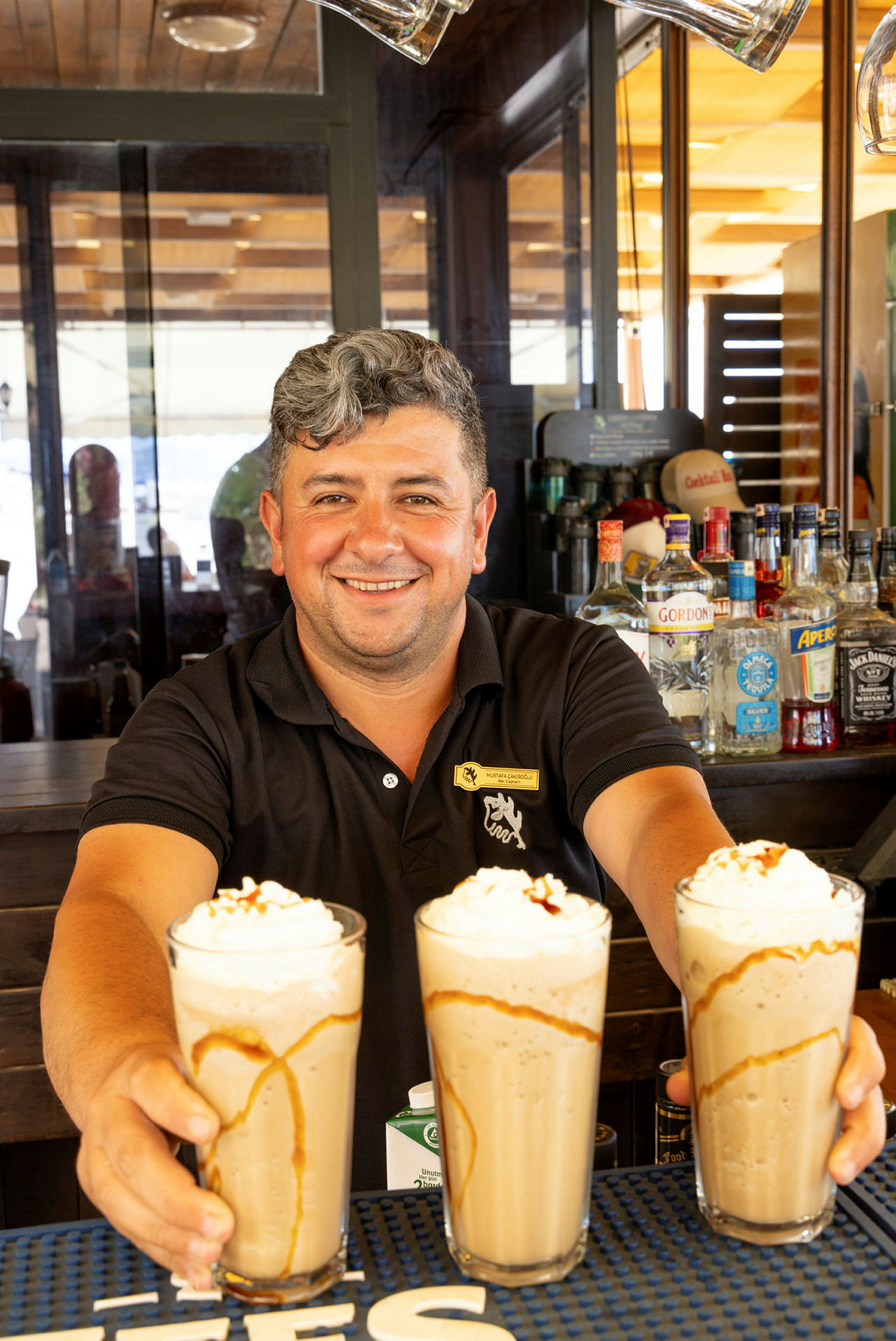 En bartender håller tre glas med milkshakes toppade med grädde och karamellsås. (AI-genererad text)
