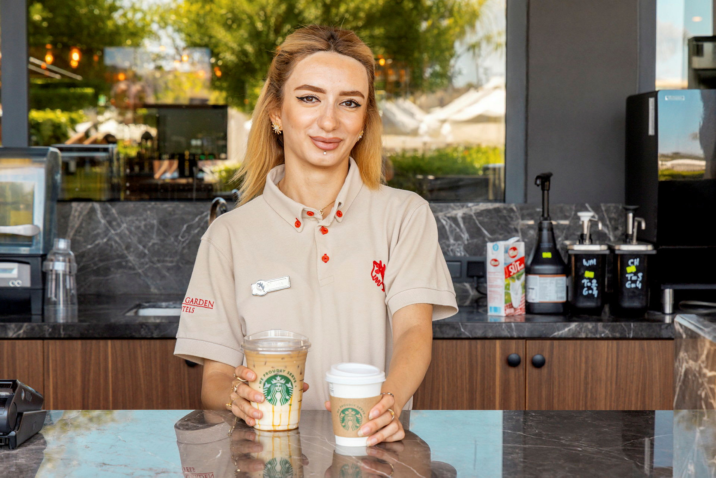 En kvinna står bakom en disk och håller i två kaffekoppar från Starbucks. (AI-genererad text)