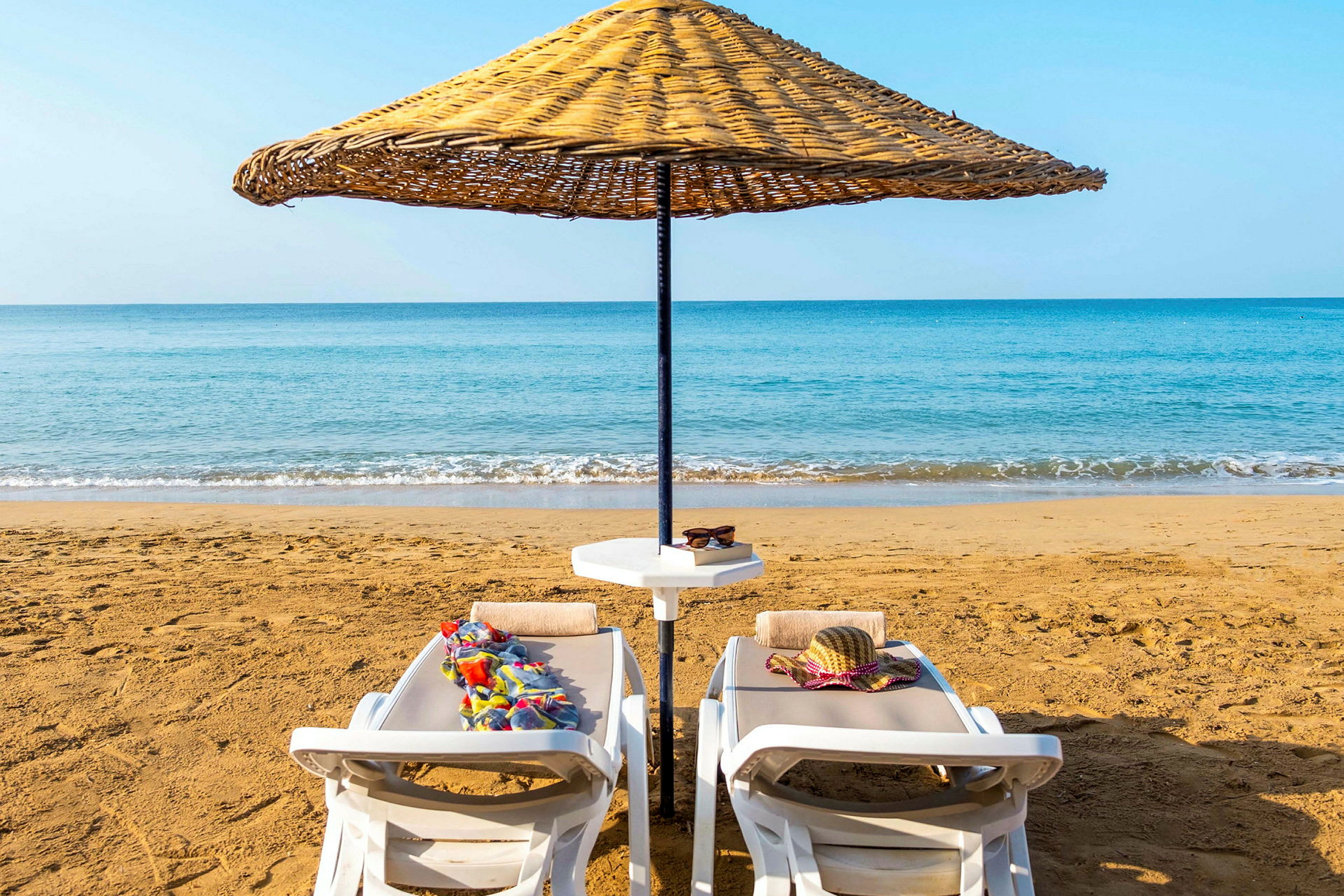 Två solstolar på en sandstrand med ett parasoll och havet i bakgrunden. (AI-genererad text)