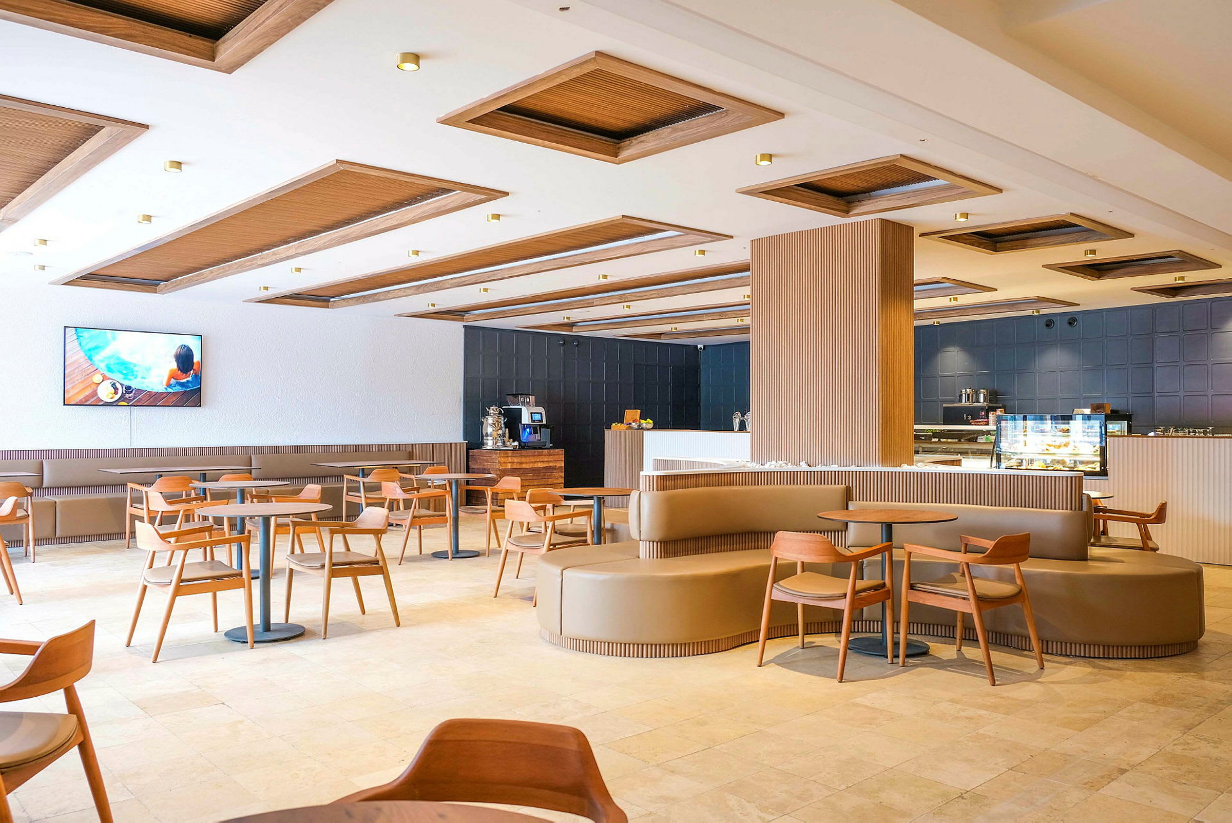 En modern restaurang med trädetaljer, bord och stolar samt en bar och en TV på väggen. (AI-genererad text)