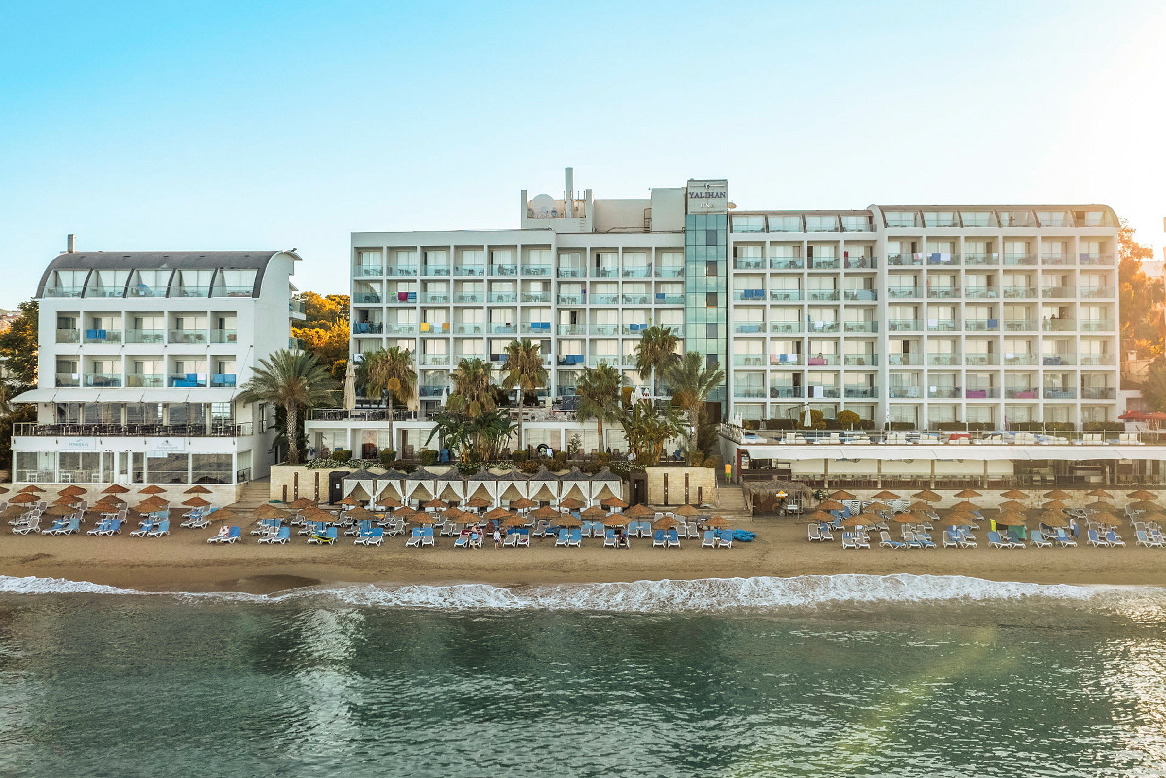 Bild av en stor vit hotellbyggnad vid en solig strand med solsängar och parasoller. (AI-genererad text)