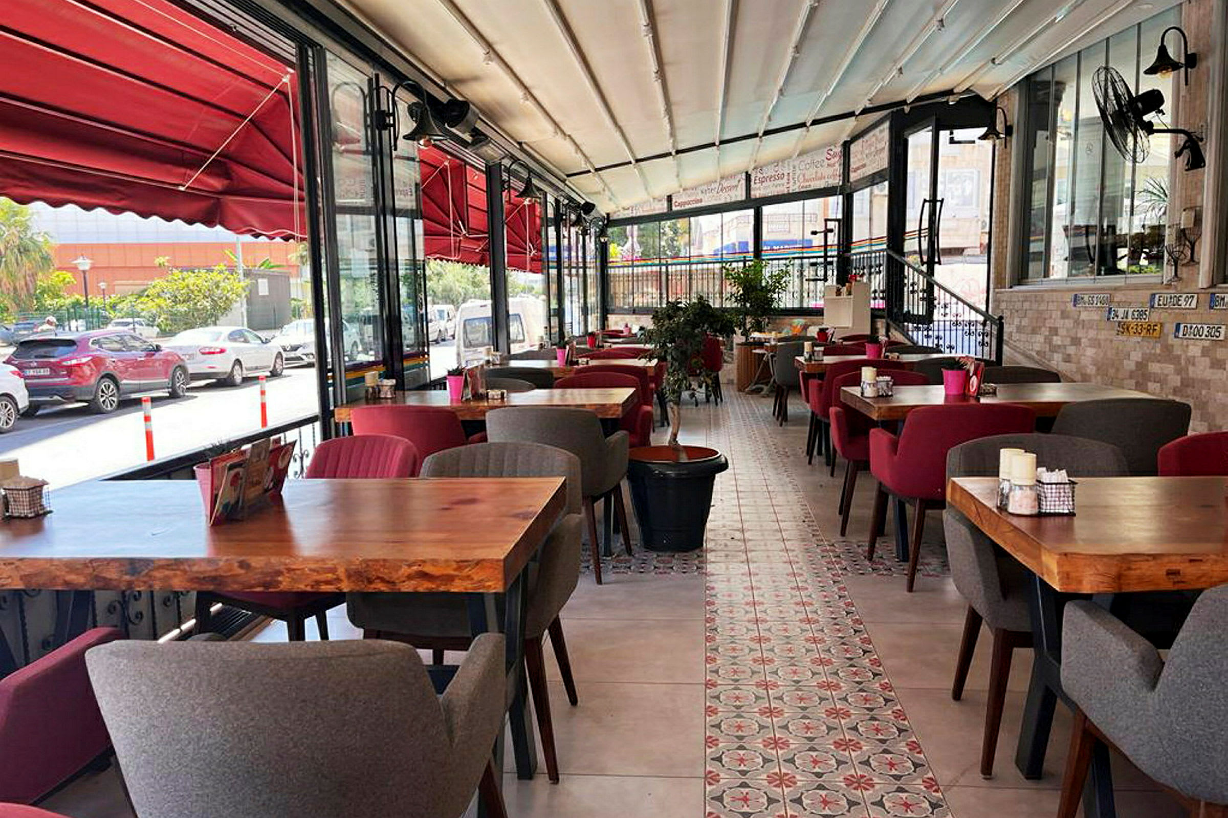 Bild av en restaurang med röd inredning, träbord och mjuka stolar. Utsikt över gatan syns genom glasfönster. (AI-genererad text)