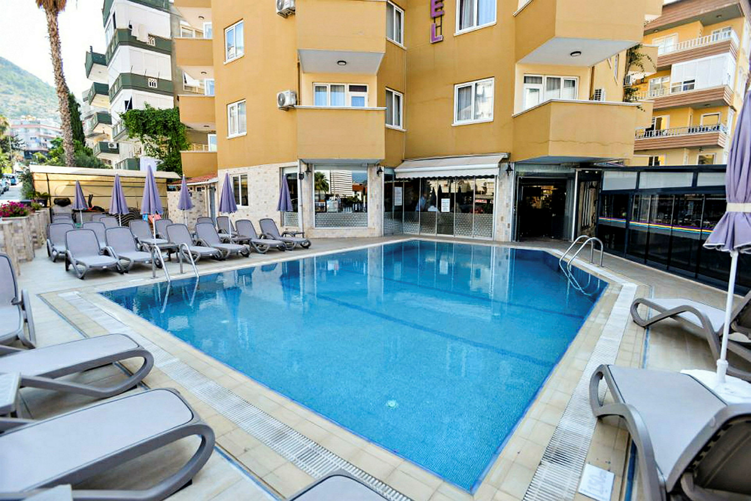 En swimmingpool utomhus omgiven av solstolar och parasoller vid en byggnad. (AI-genererad text)