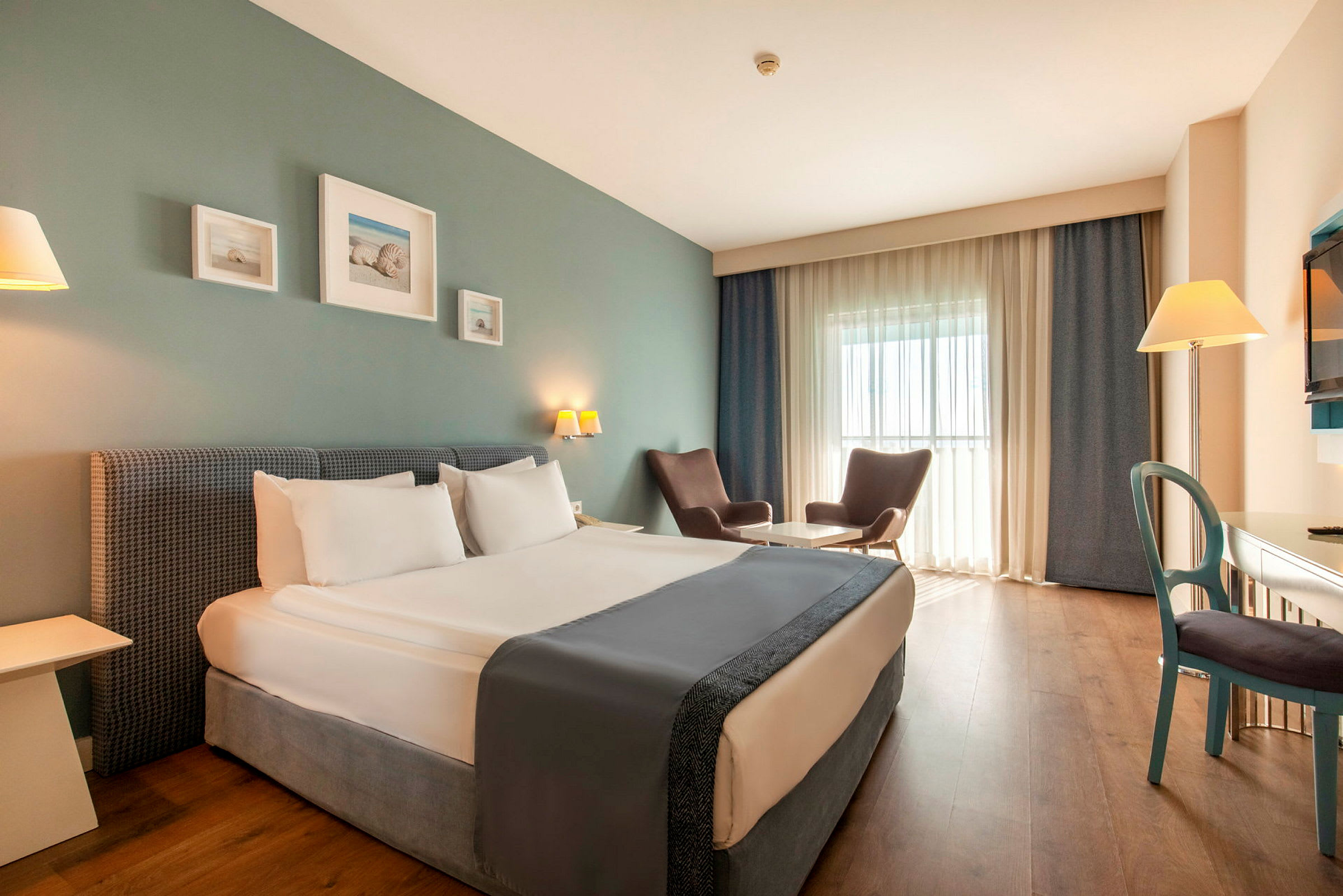 Ett hotellrum med en dubbelsäng, två fåtöljer vid ett bord, ett skrivbord och en TV. (AI-genererad text)
