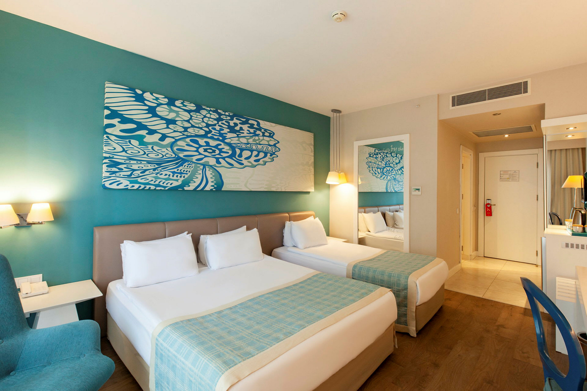 Två sängar med vita sängkläder i ett hotellrum, med turkosa detaljer och modern inredning. (AI-genererad text)