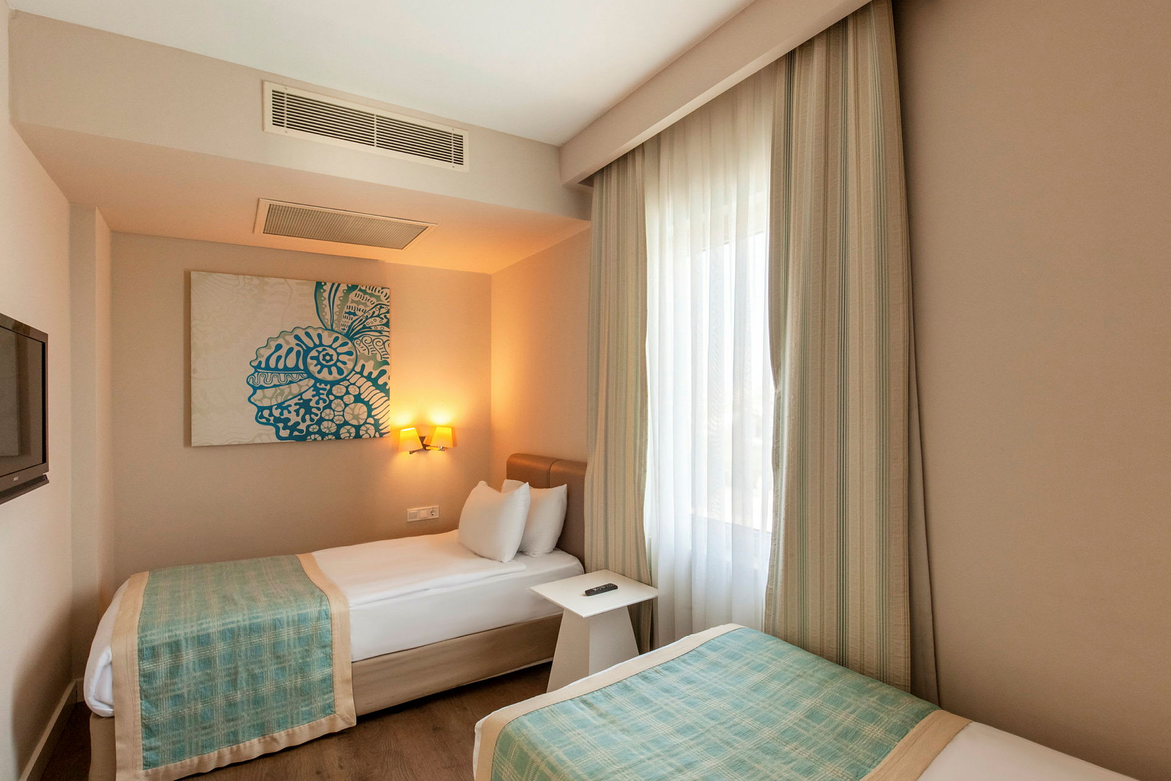 Hotellrum med två enkelsängar, väggmonterad konst och ett fönster med gardiner. (AI-genererad text)