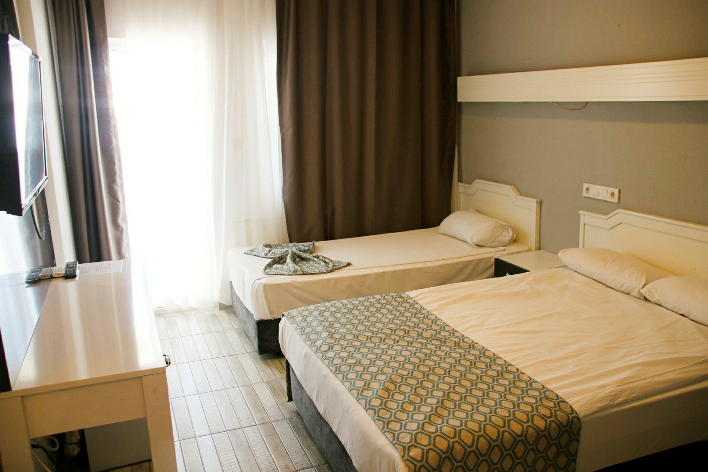Ett hotellrum med två sängar, en större och en mindre, samt ett bord framför en TV på väggen. (AI-genererad text)