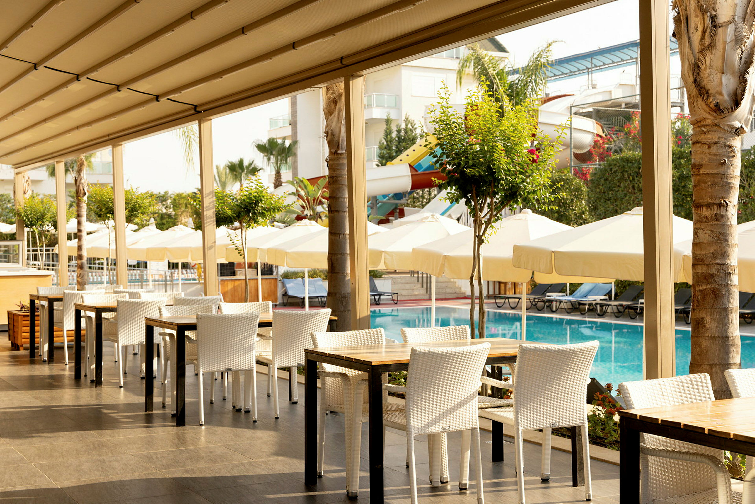 Utomhusrestaurang vid en pool med parasoller och solstolar i bakgrunden. (AI-genererad text)