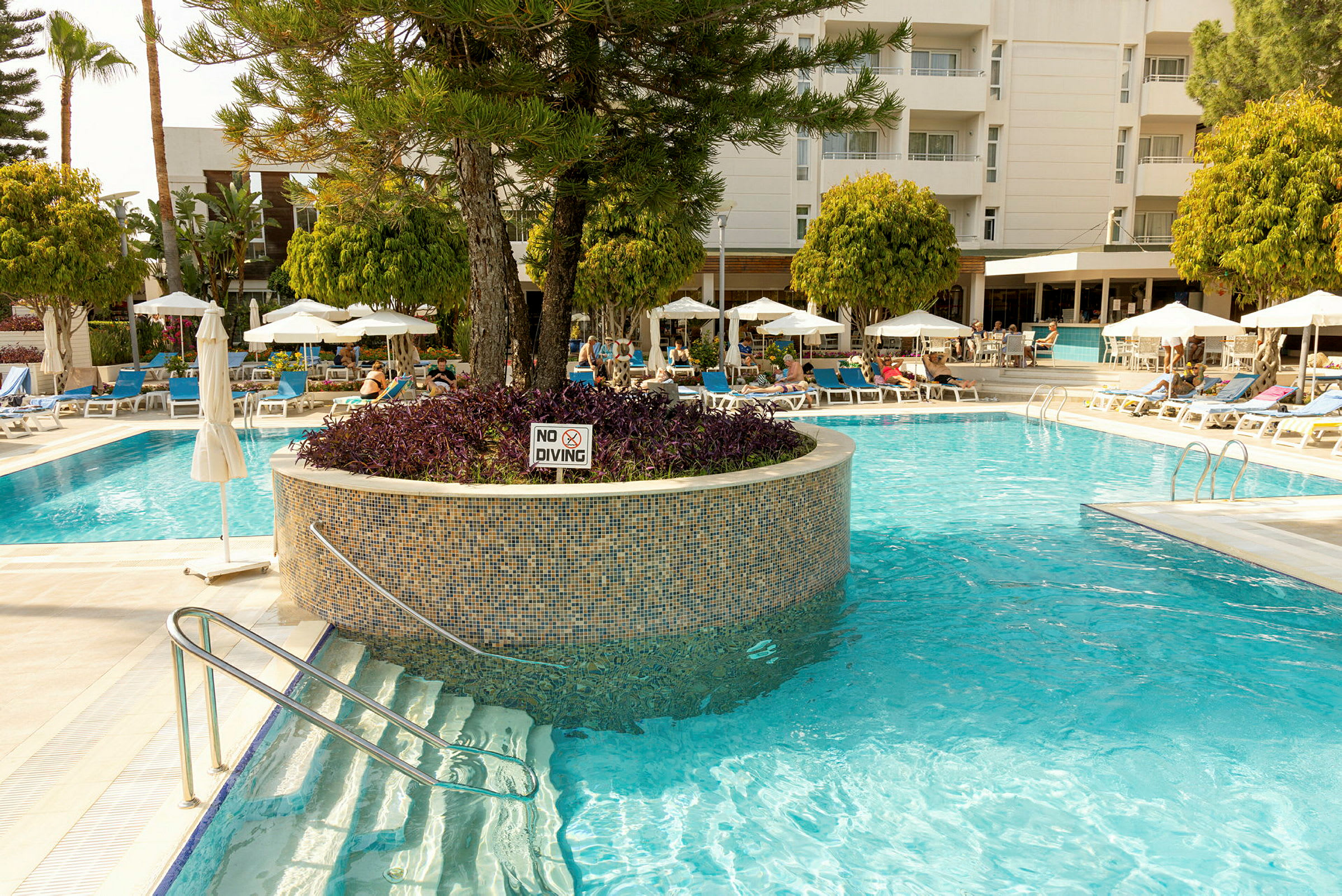 En hotellpool omgiven av solstolar och parasoller. (AI-genererad text)