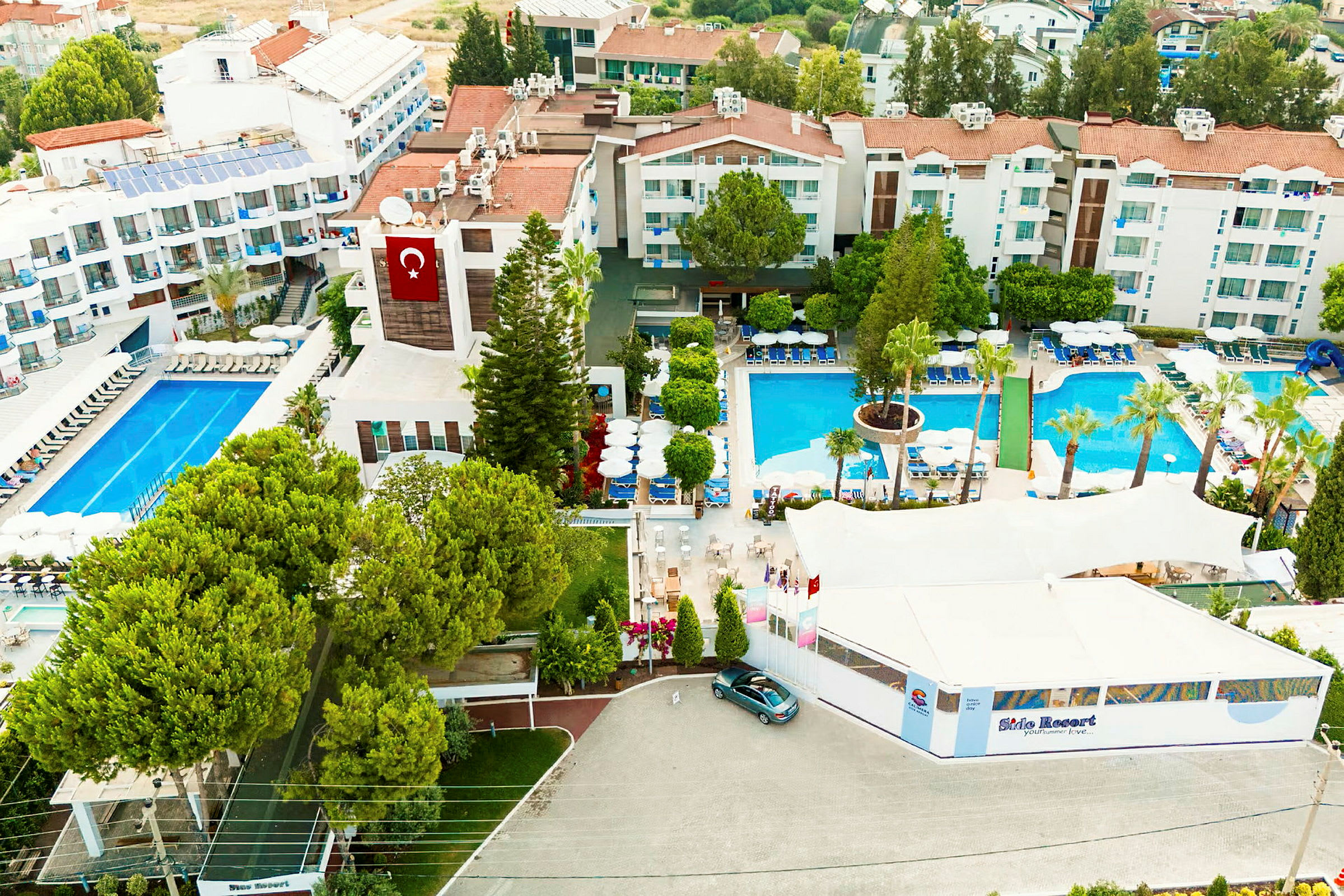 En flygbild på ett hotellområde med pooler, byggnader och gröna träd. (AI-genererad text)
