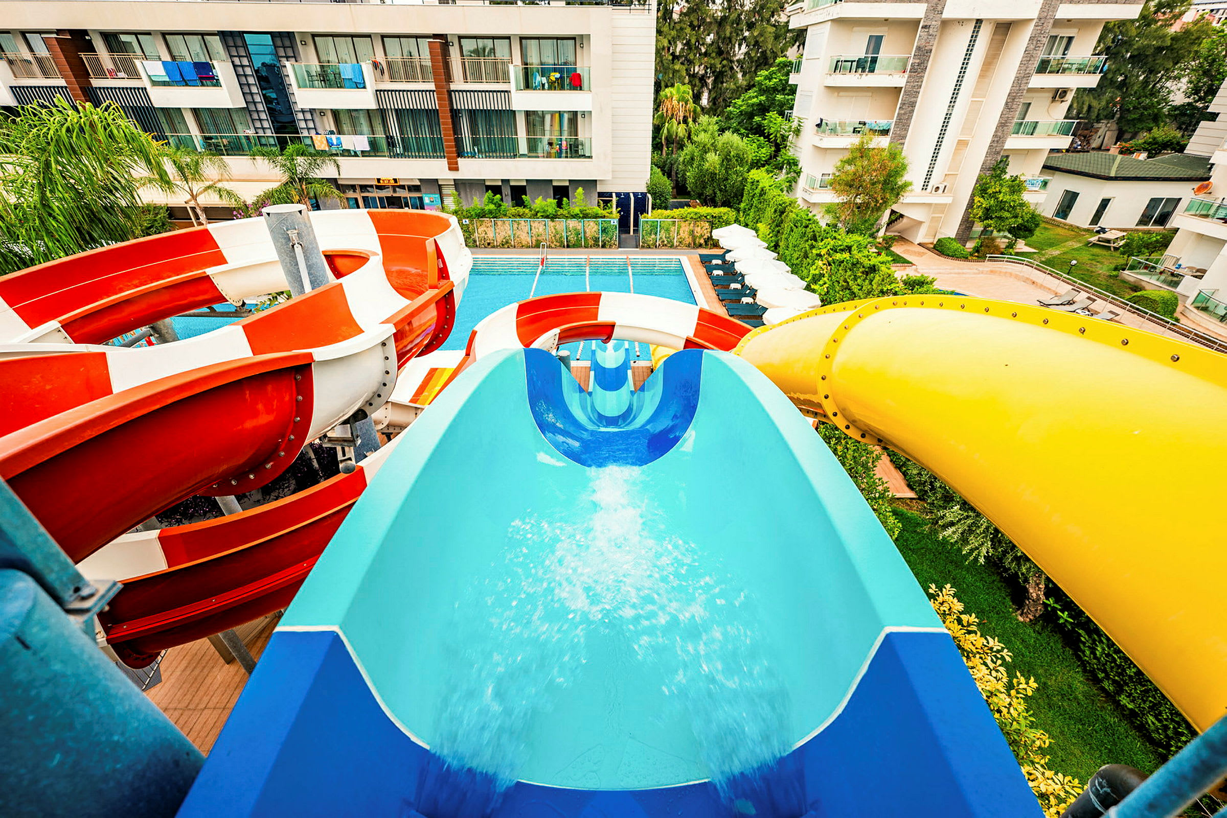 Vattenrutschkanor med olika färger leder till en pool på en hotellanläggning. (AI-genererad text)