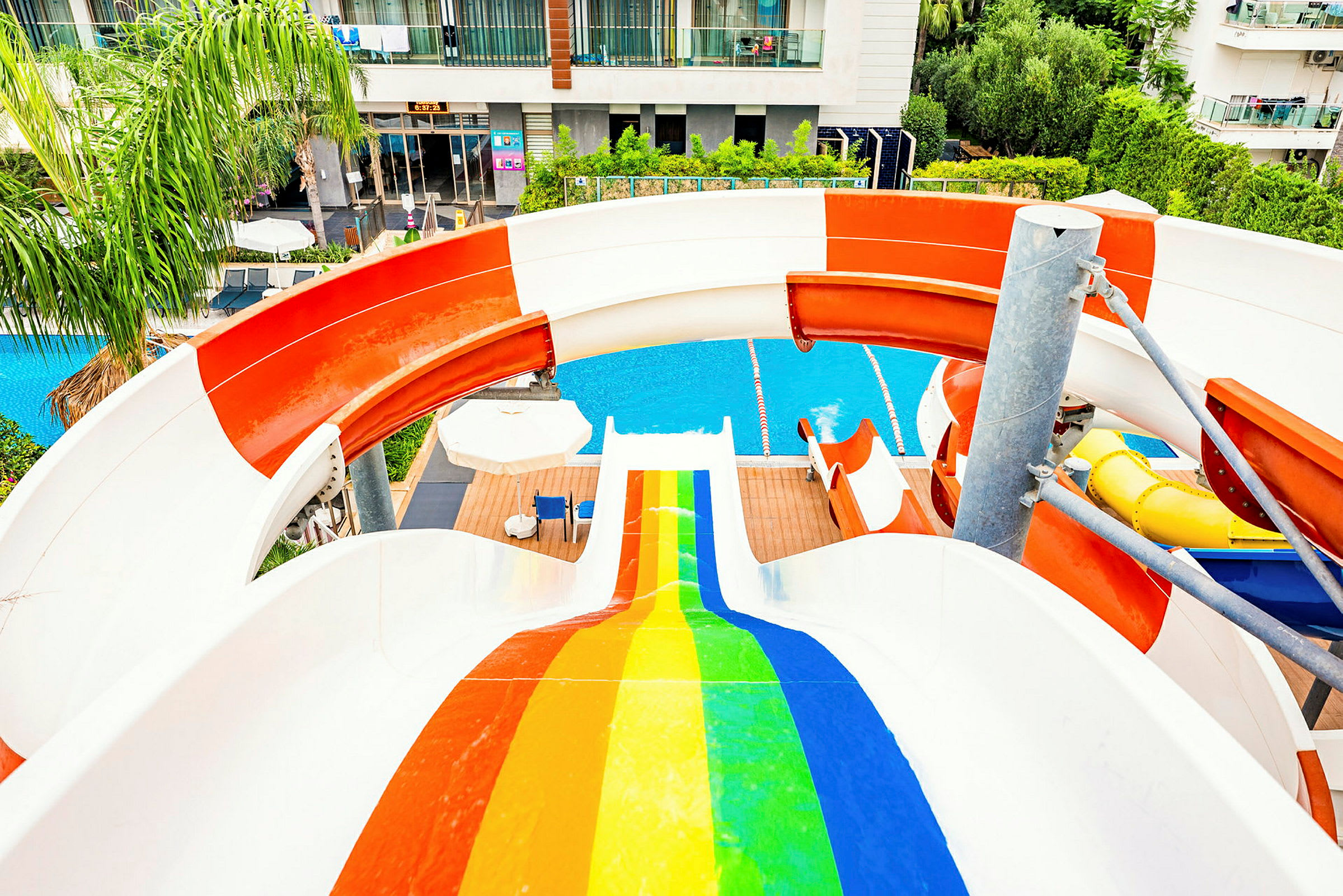 En vattenrutschkana med regnbågsfärger som leder ner till en pool vid ett hotell. (AI-genererad text)