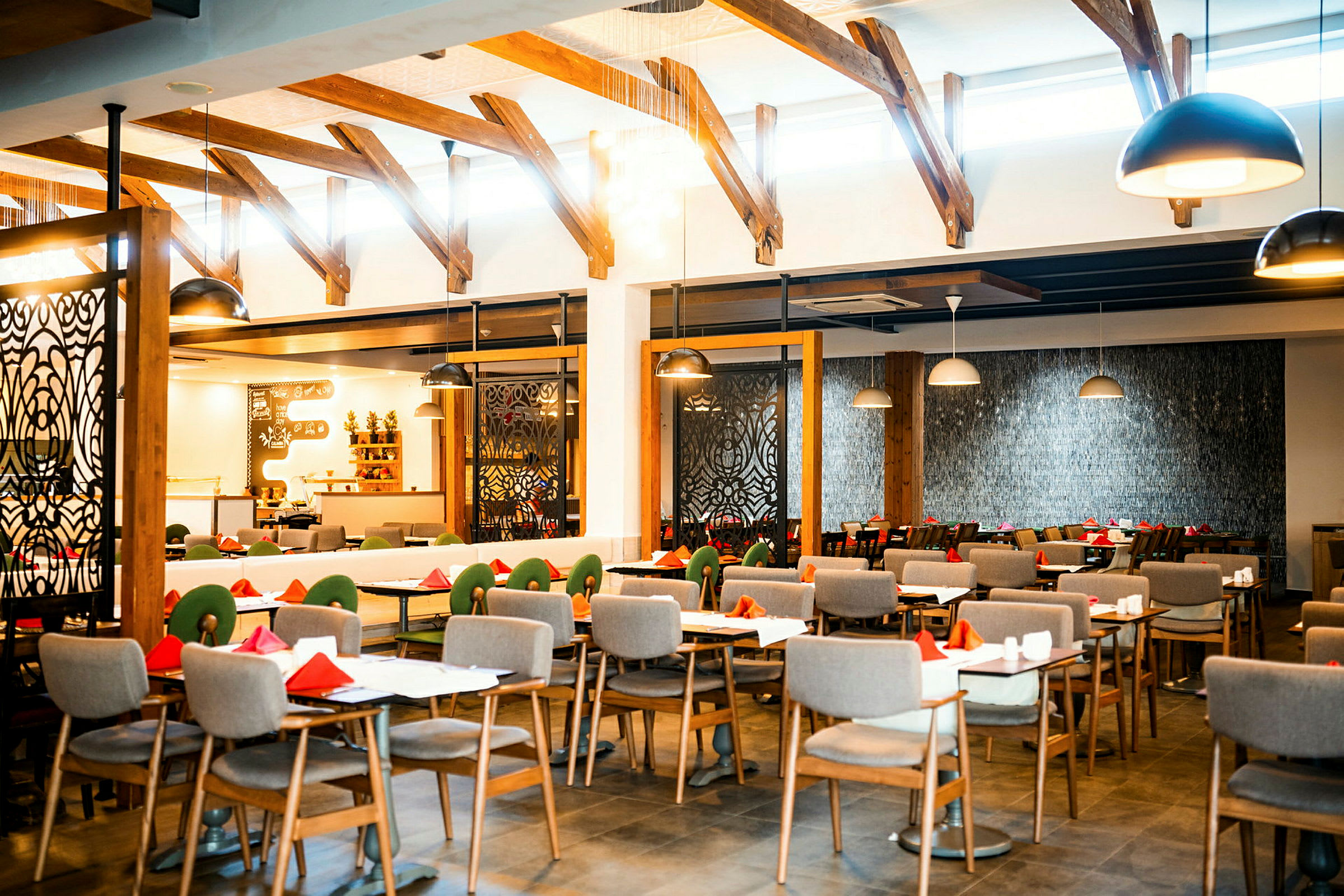 Interiören av en restaurang med uppställda dukade bord och stolar, med takbjälkar och modernt designade lampor. (AI-genererad text)