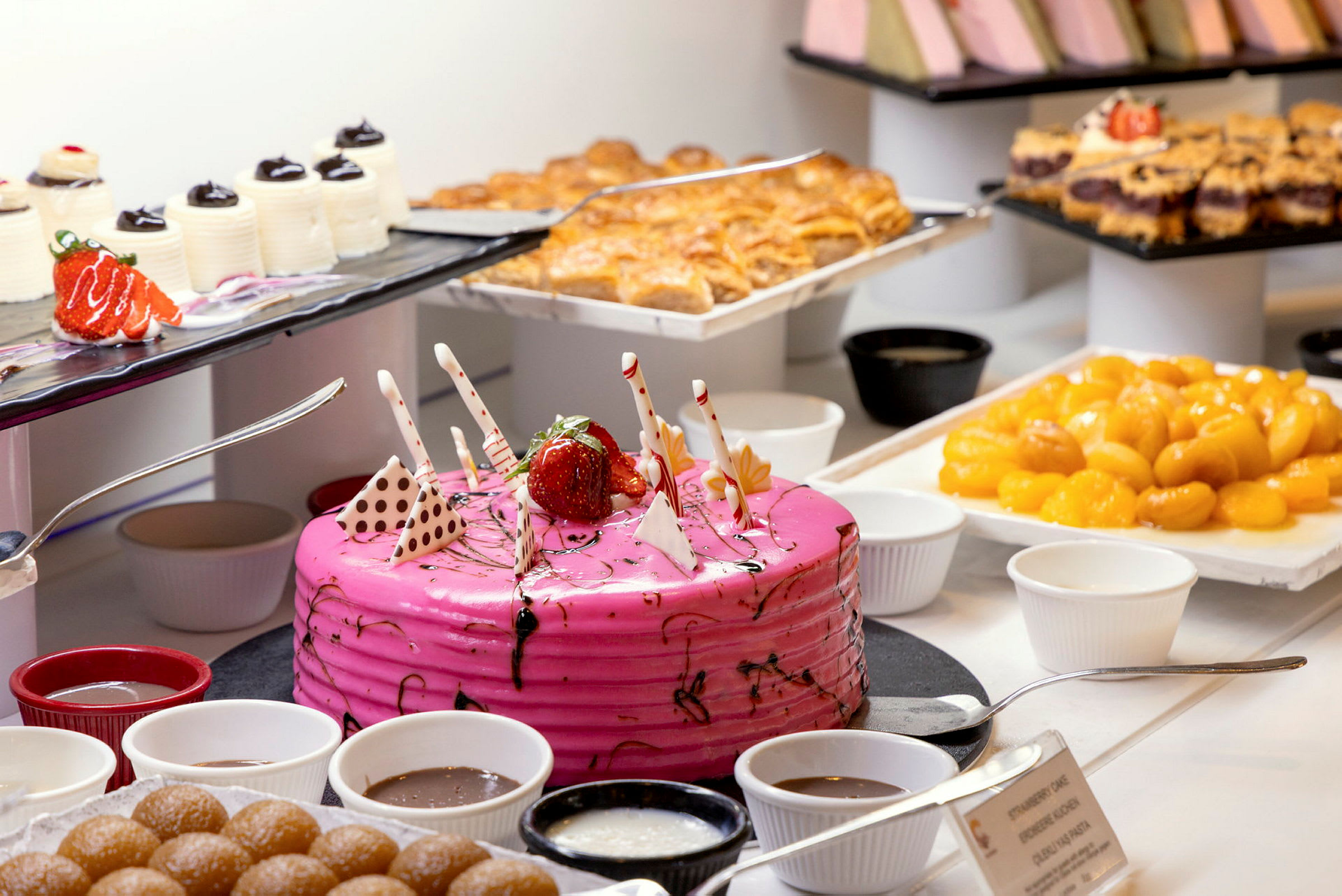 Ett bord med olika desserter inklusive en rosa tårta, bakverk och skålar med chokladsås. (AI-genererad text)