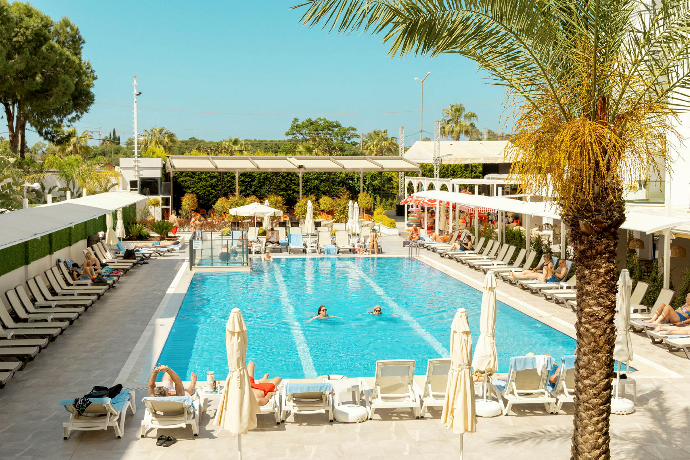 Bild av en pool omgiven av solstolar och parasoller, med personer som badar och solar. (AI-genererad text)
