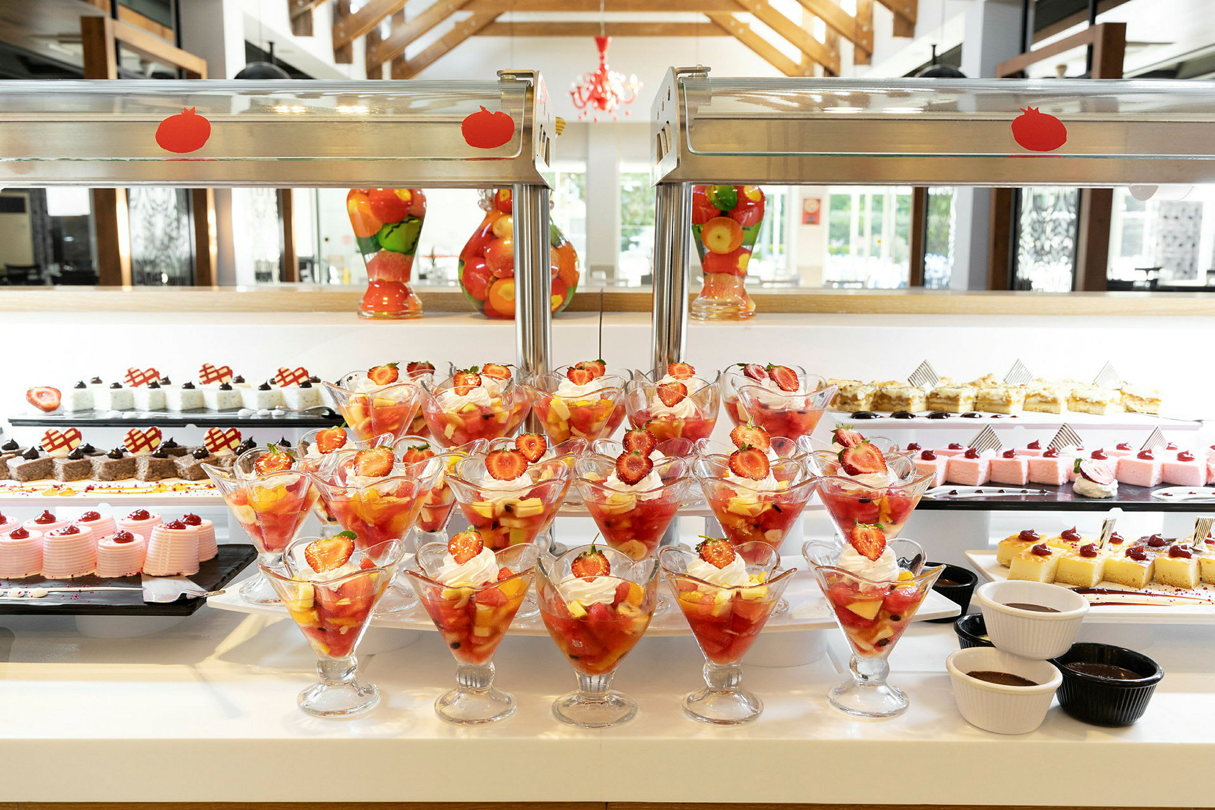 Fruktcocktail med jordgubbar och vispad grädde i glas framför ett dessertbord. (AI-genererad text)