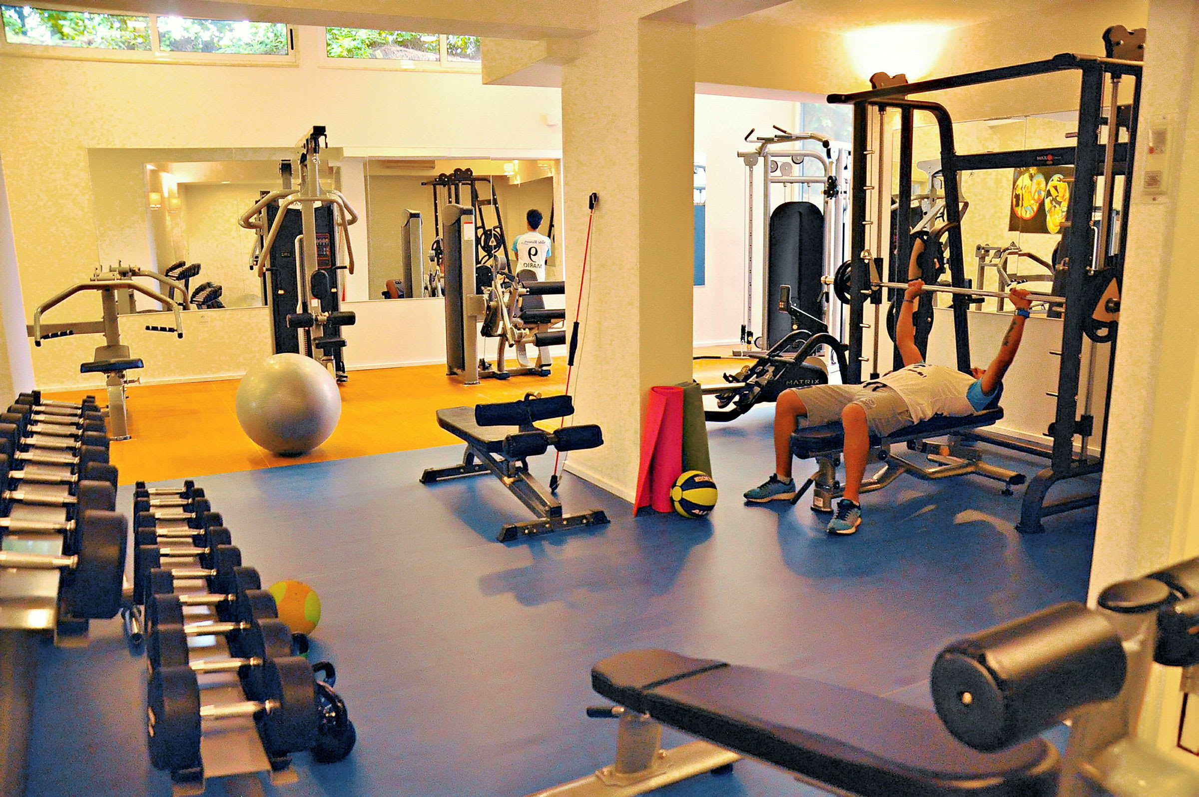 Ett gym med träningsutrustning och en person som lyfter vikter på en maskin. (AI-genererad text)