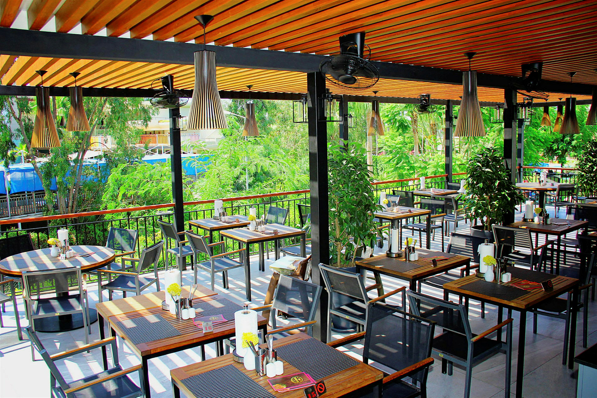 Utomhusrestaurang med bord och stolar, omgivna av grönska. (AI-genererad text)