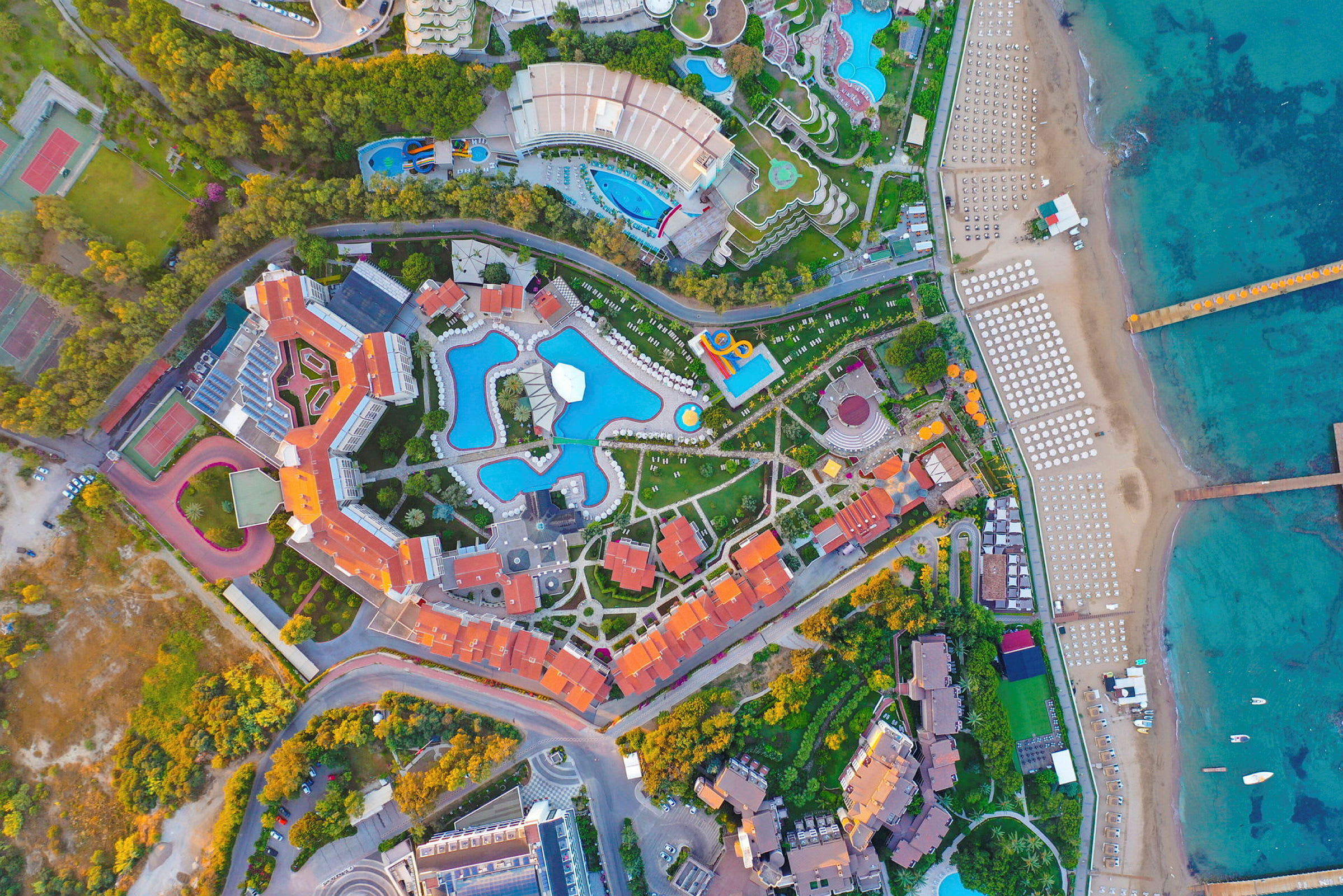 Flygfoto över ett semesteranläggning med pooler och strand. (AI-genererad text)