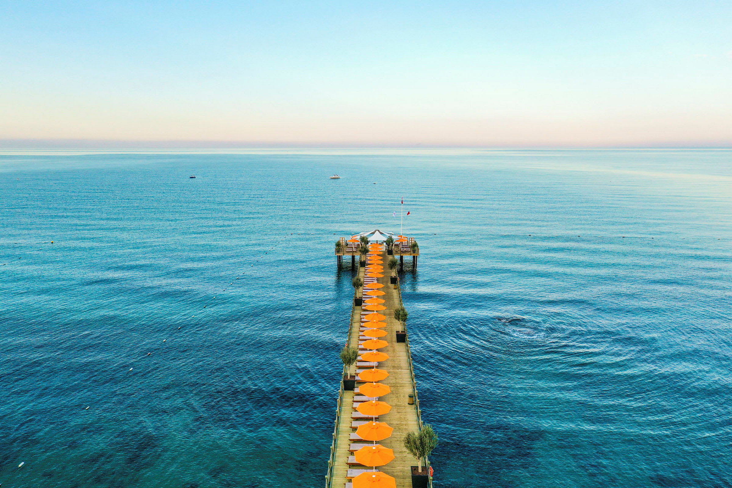 En brygga med orange parasoller som leder ut i det blå havet under en klar himmel. (AI-genererad text)