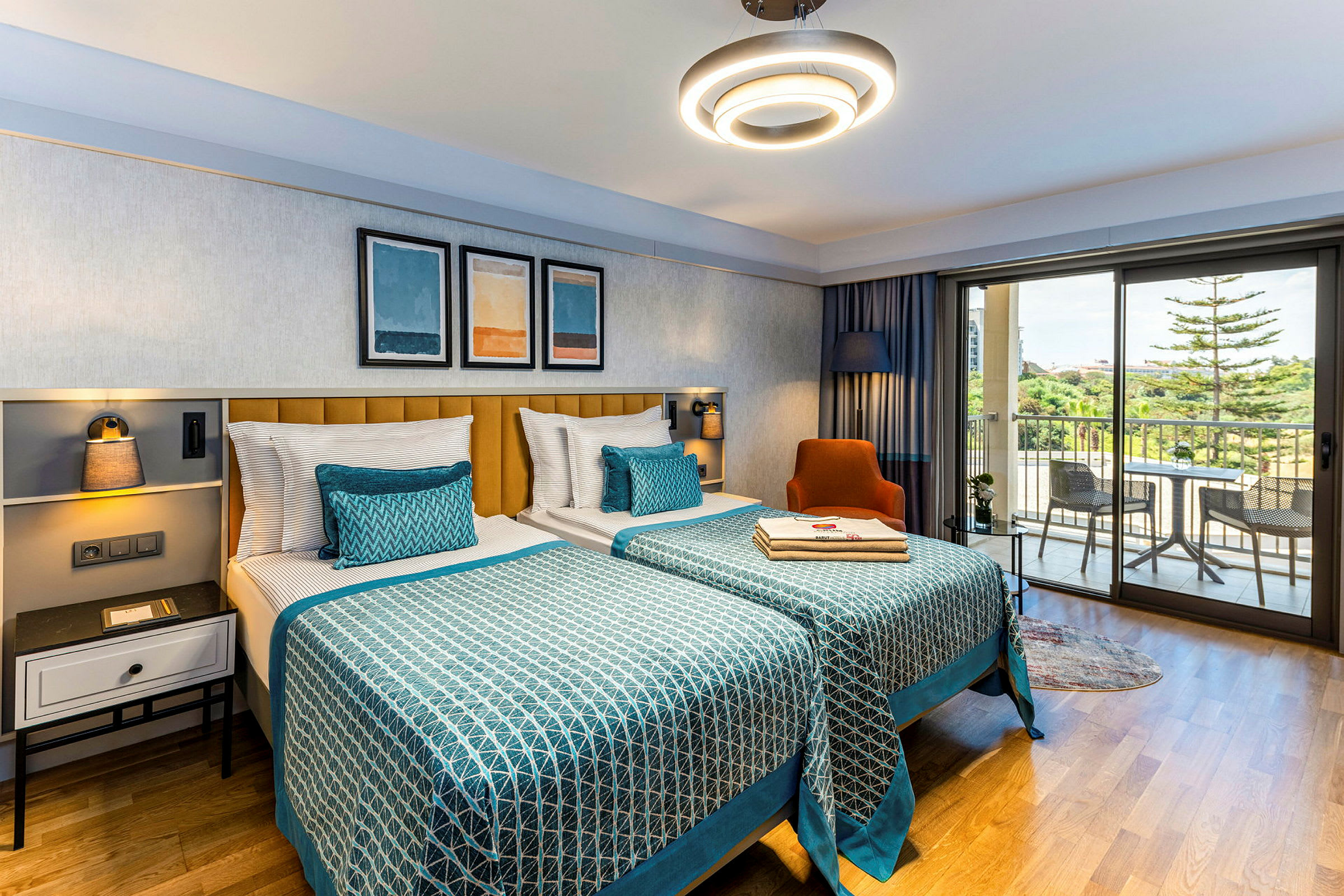 Hotellrum med två sängar bredvid varandra och dekorerade överkast, fönster med utsikt på en balkong utomhus. (AI-genererad text)
