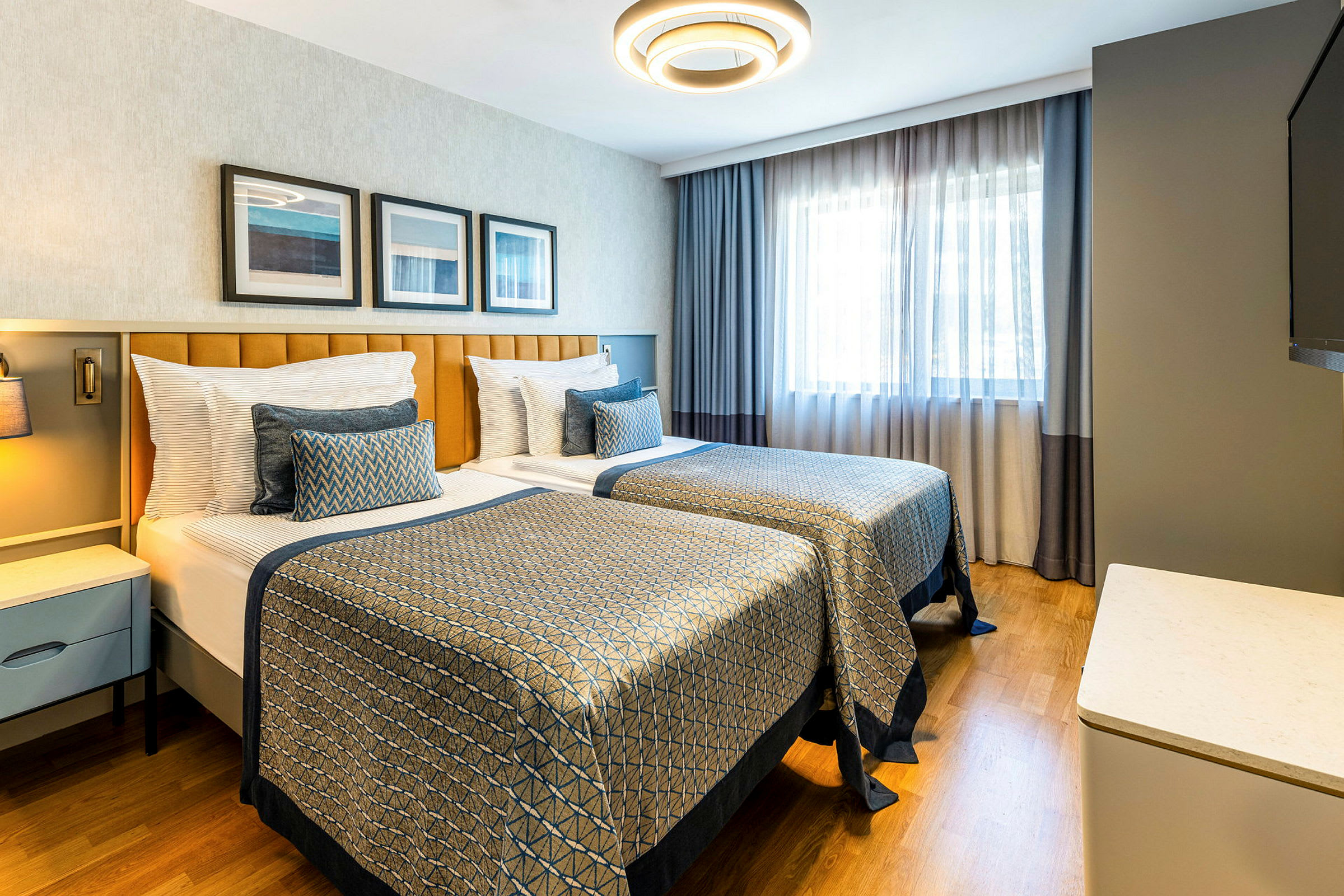 Ett hotellrum med två enkelsängar, modern inredning och naturligt ljus från ett fönster. (AI-genererad text)