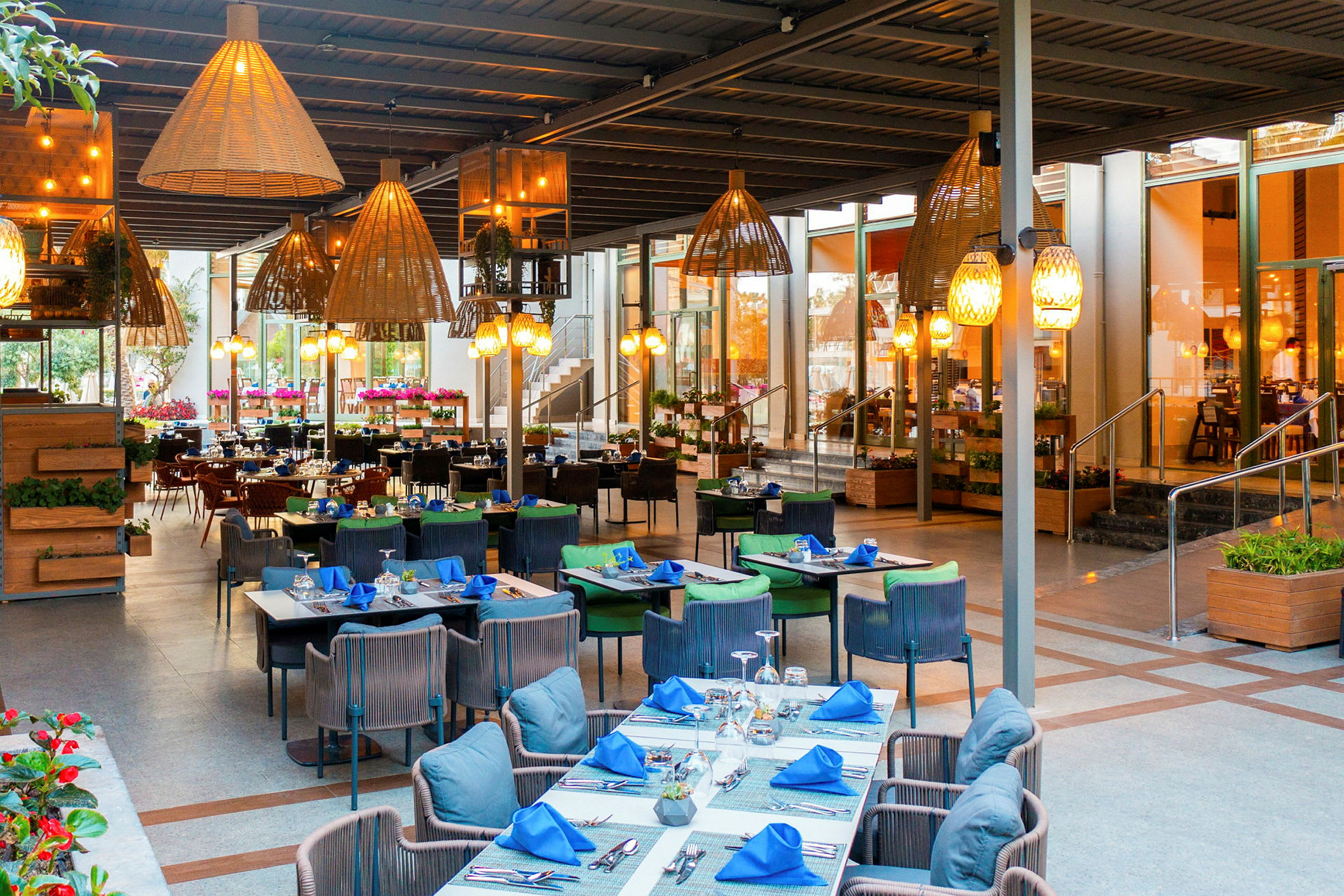 En restaurang med bord och stolar under tak, dekorerad med hängande lampor och växter. (AI-genererad text)
