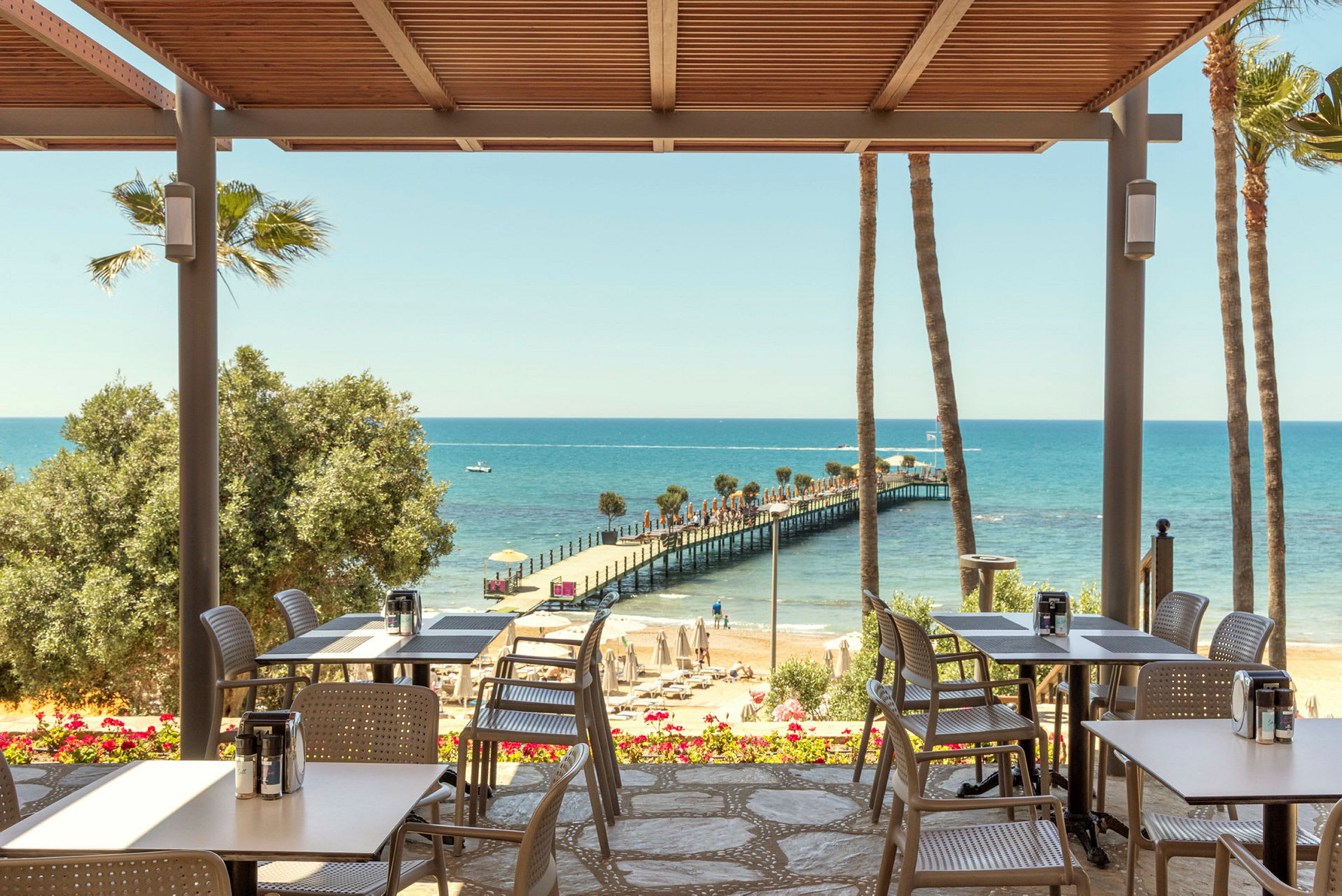 En restaurang med utsikt över en strand och en brygga som sträcker sig ut i havet. (AI-genererad text)