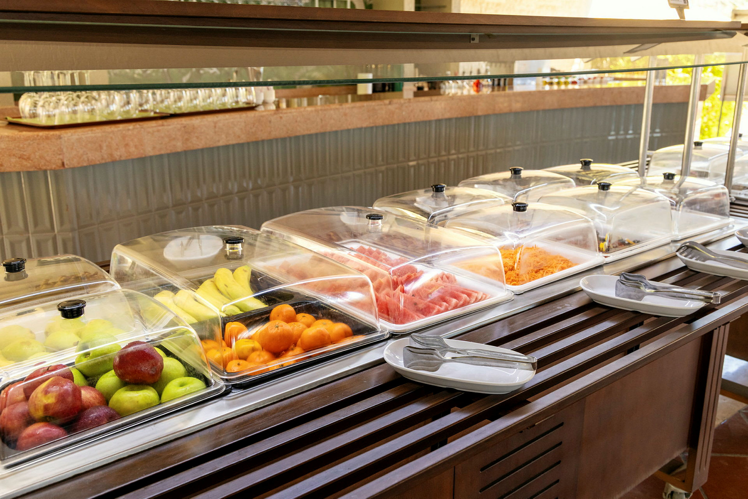 Buffébord med frukt, grönsaker och kalla rätter under genomskinliga lock. (AI-genererad text)