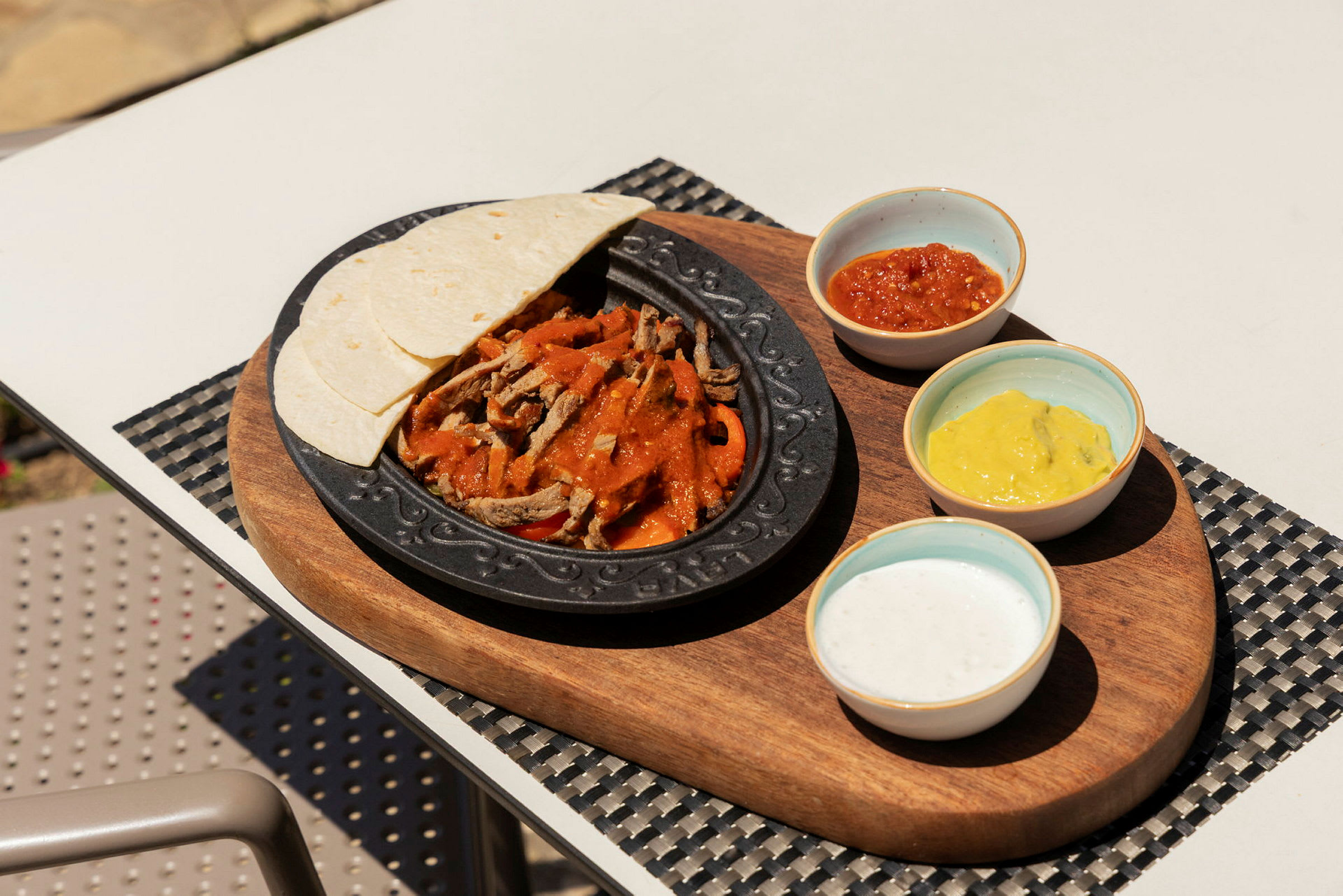 En tallrik med kött, grönsaker och såser samt tortillabröd på en träbricka. (AI-genererad text)