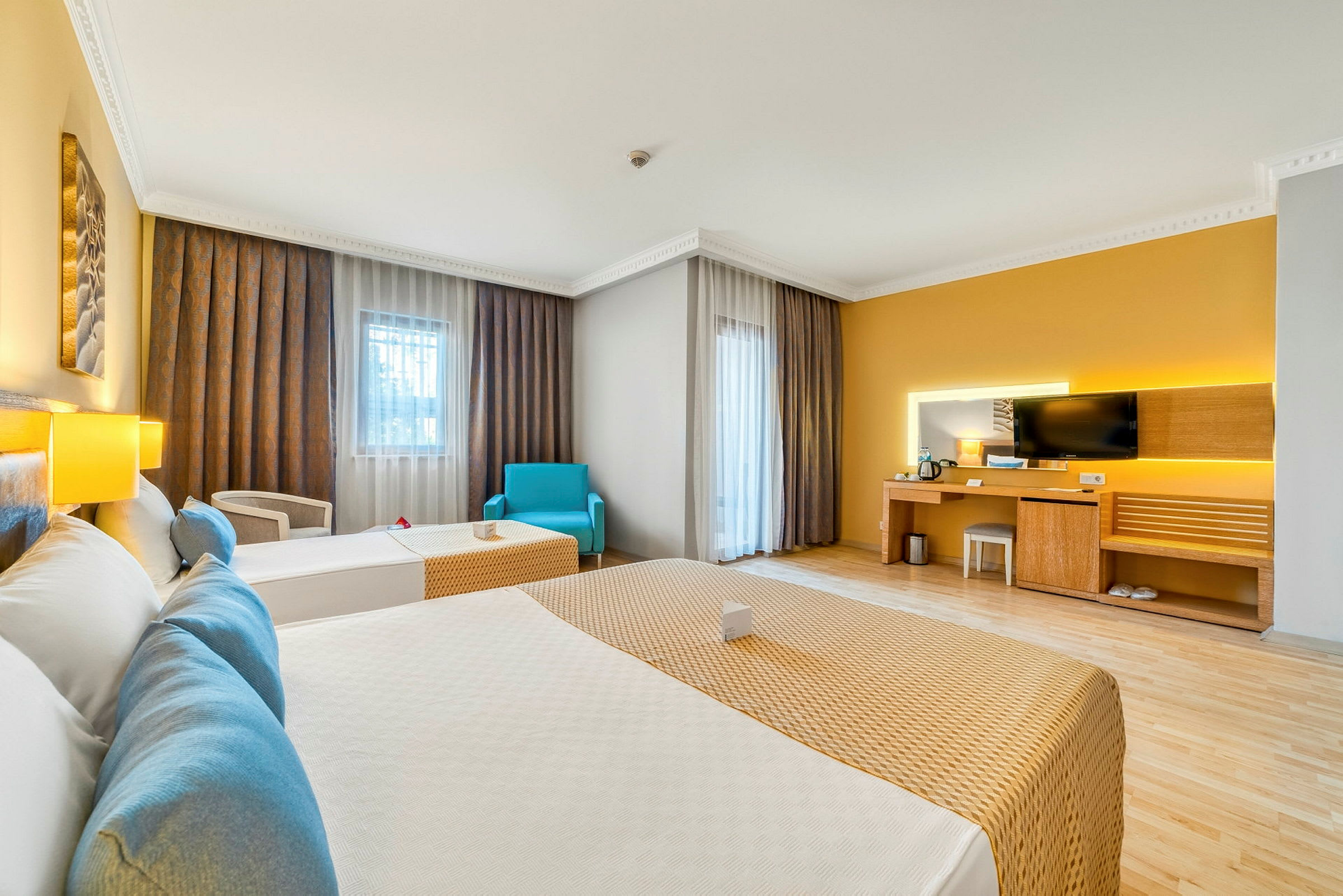 Ett hotellrum med två bäddar, en skrivbordshörna med TV och stora fönster med gardiner. (AI-genererad text)
