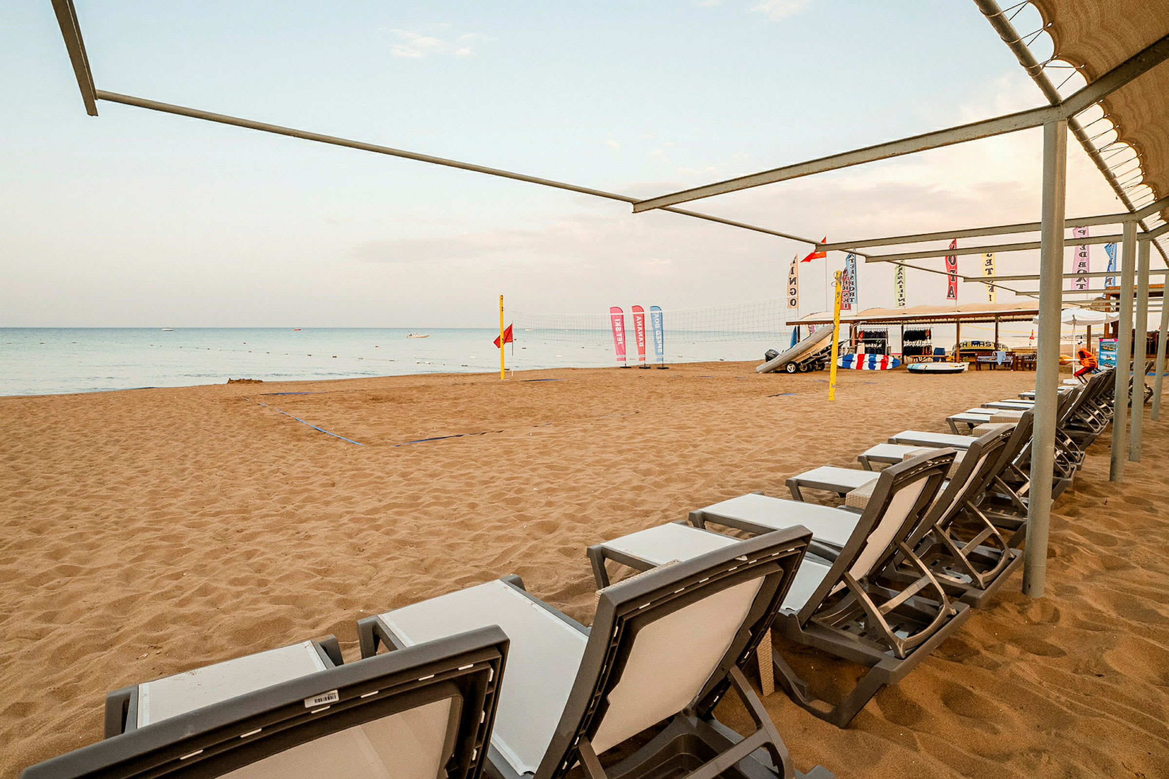 En sandstrand med solstolar, volleybollnät och skyltar vid havet. (AI-genererad text)