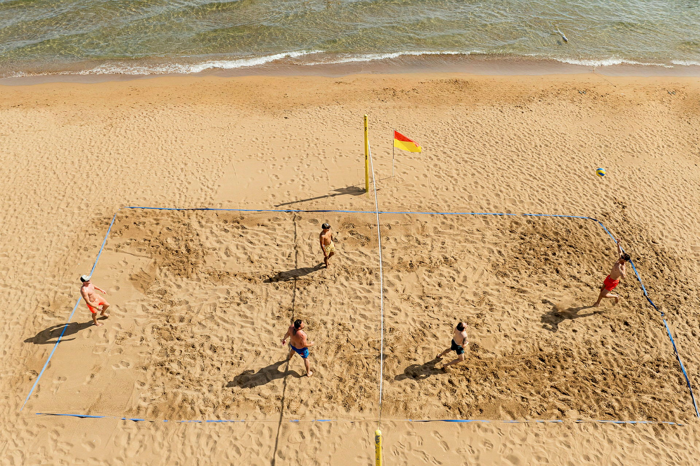 Fyra personer spelar beachvolleyboll på en sandstrand nära havet. (AI-genererad text)