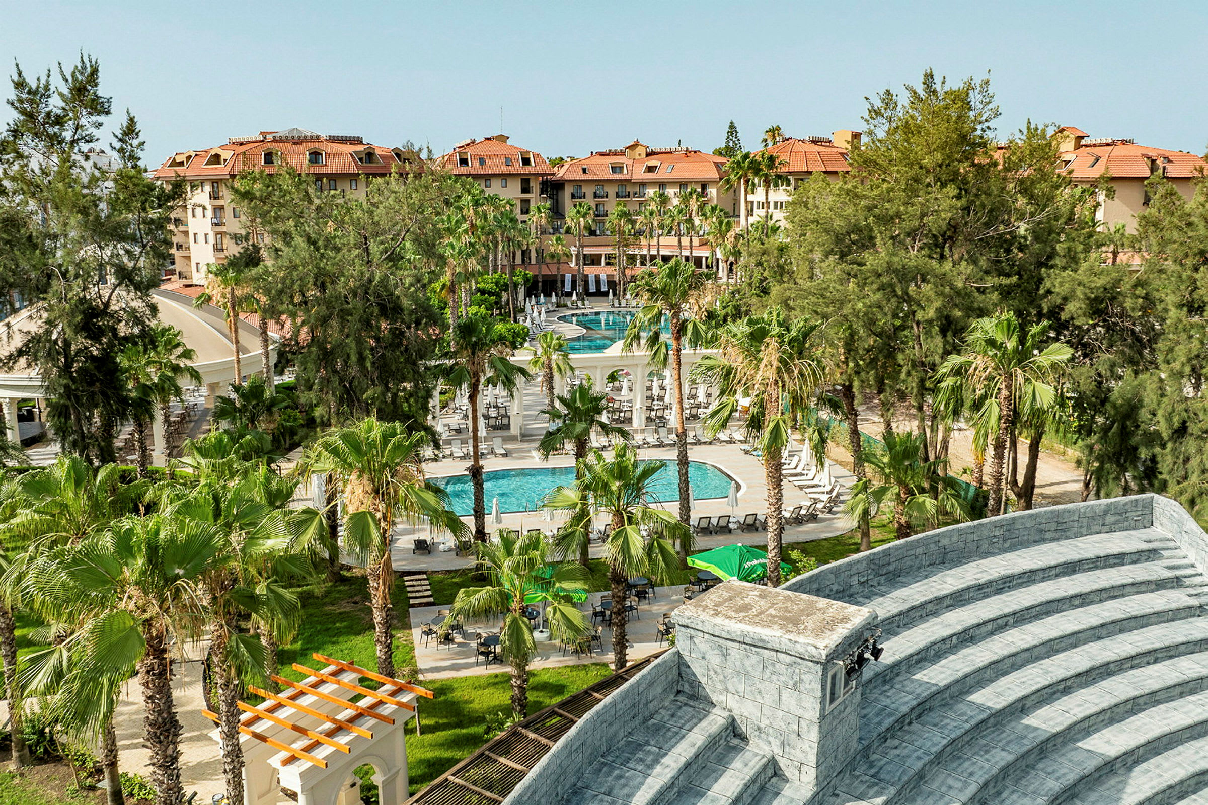 Vy över hotellområde med byggnader, grönska och pool. (AI-genererad text)