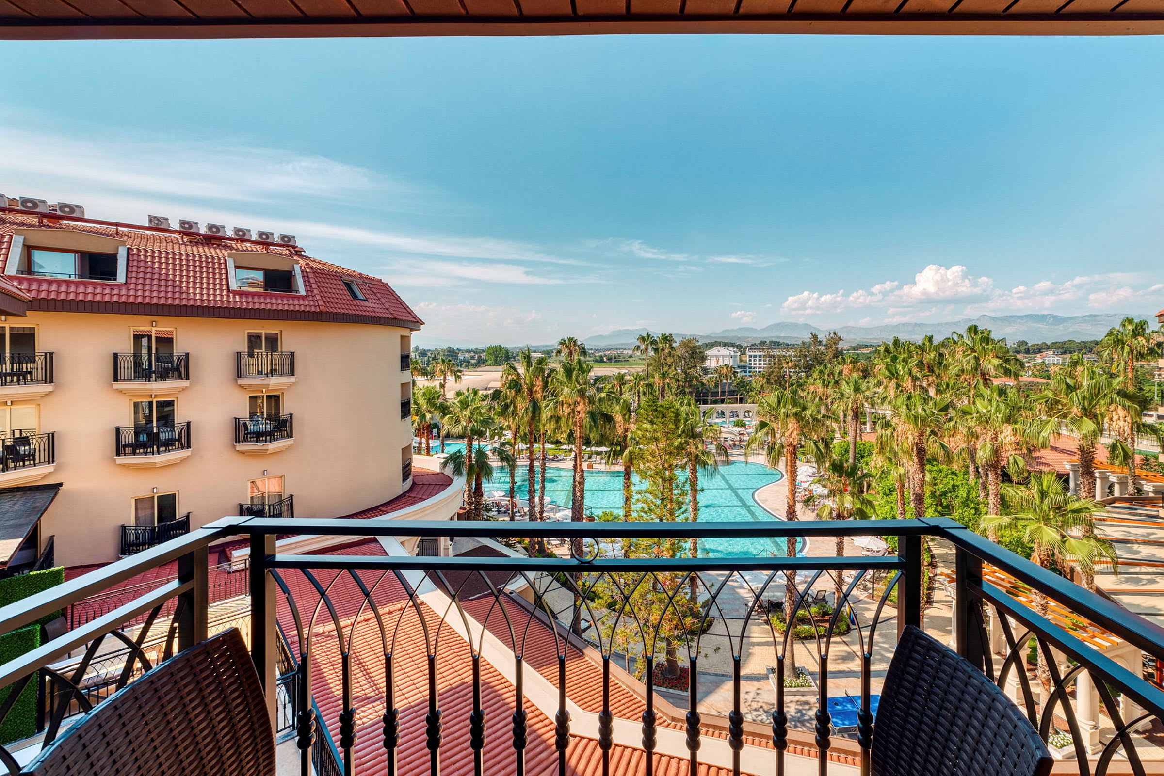 Utsikt från en balkong över en hotellbyggnad, en pool och palmträd. (AI-genererad text)