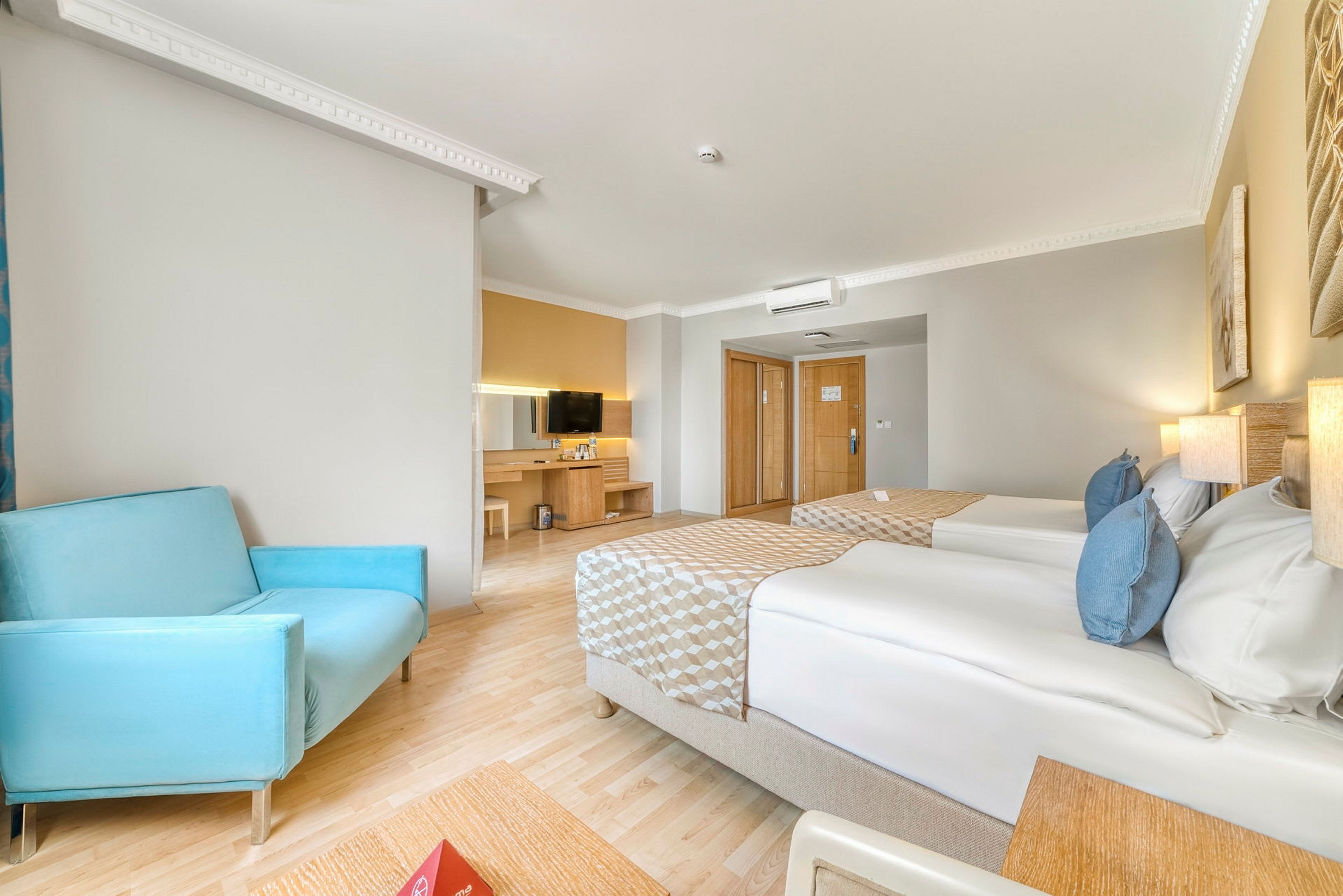 Ett hotellrum med två enkelsängar, en blå stol och en TV på en byrå. (AI-genererad text)