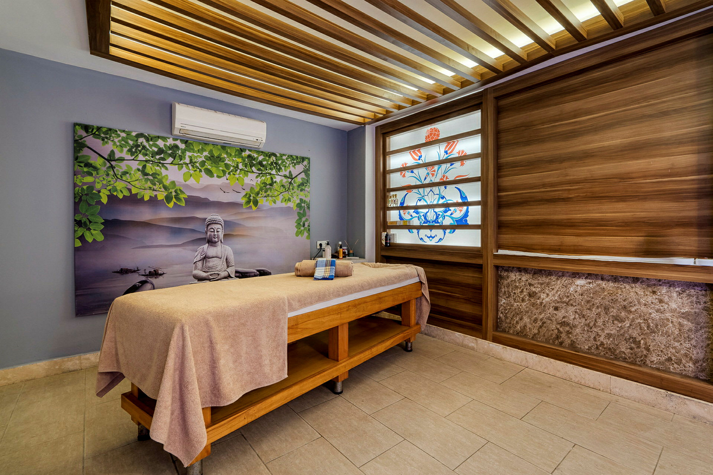 Ett behandlingsrum med en massagebänk täckt med en handduk och dekorationer på väggarna som ett landskapsmålning och träpaneler. (AI-genererad text)