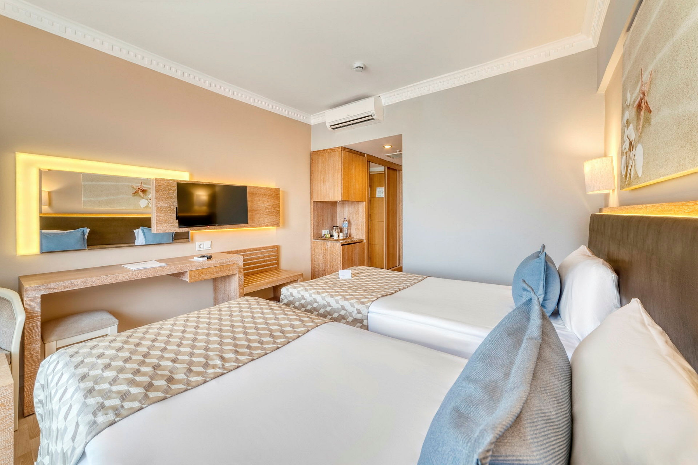Hotellrum med två enkelsängar, skrivbord, TV och ljus inredning. (AI-genererad text)