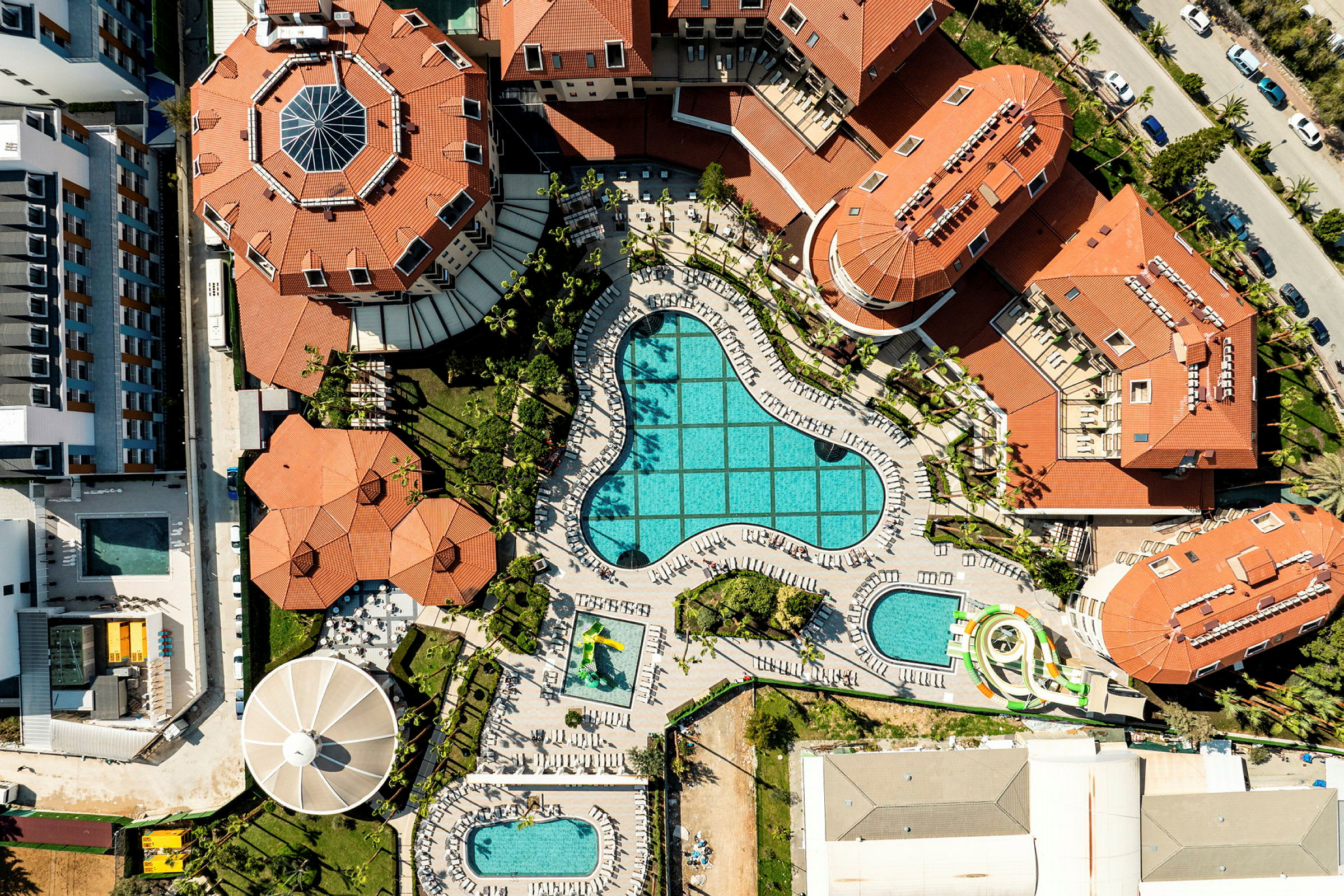Flygbild över ett hotellområde med flera byggnader och pooler. (AI-genererad text)