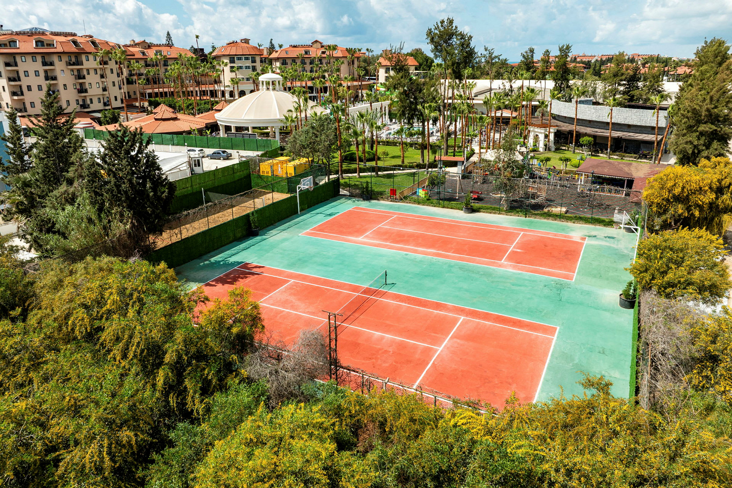 Bild av två tennisbanor omgivna av grönområden och byggnader i bakgrunden. (AI-genererad text)