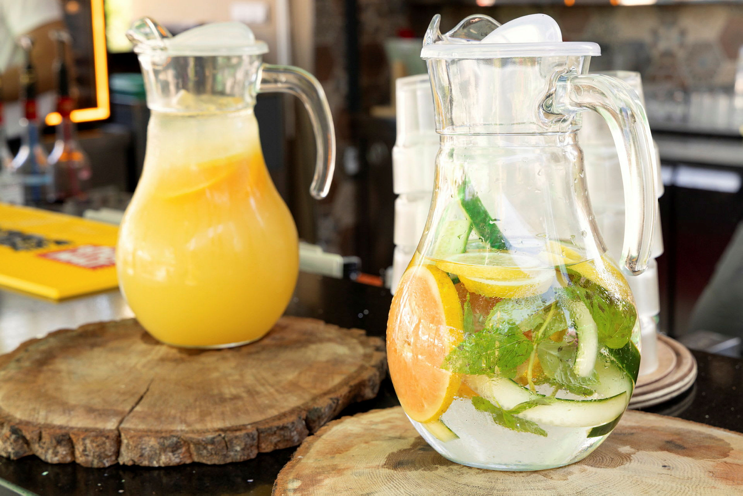 Två karaffer med drycker, en med apelsinjuice och en med smaksatt vatten med citrus och örter, står på träplattor på ett bord. (AI-genererad text)