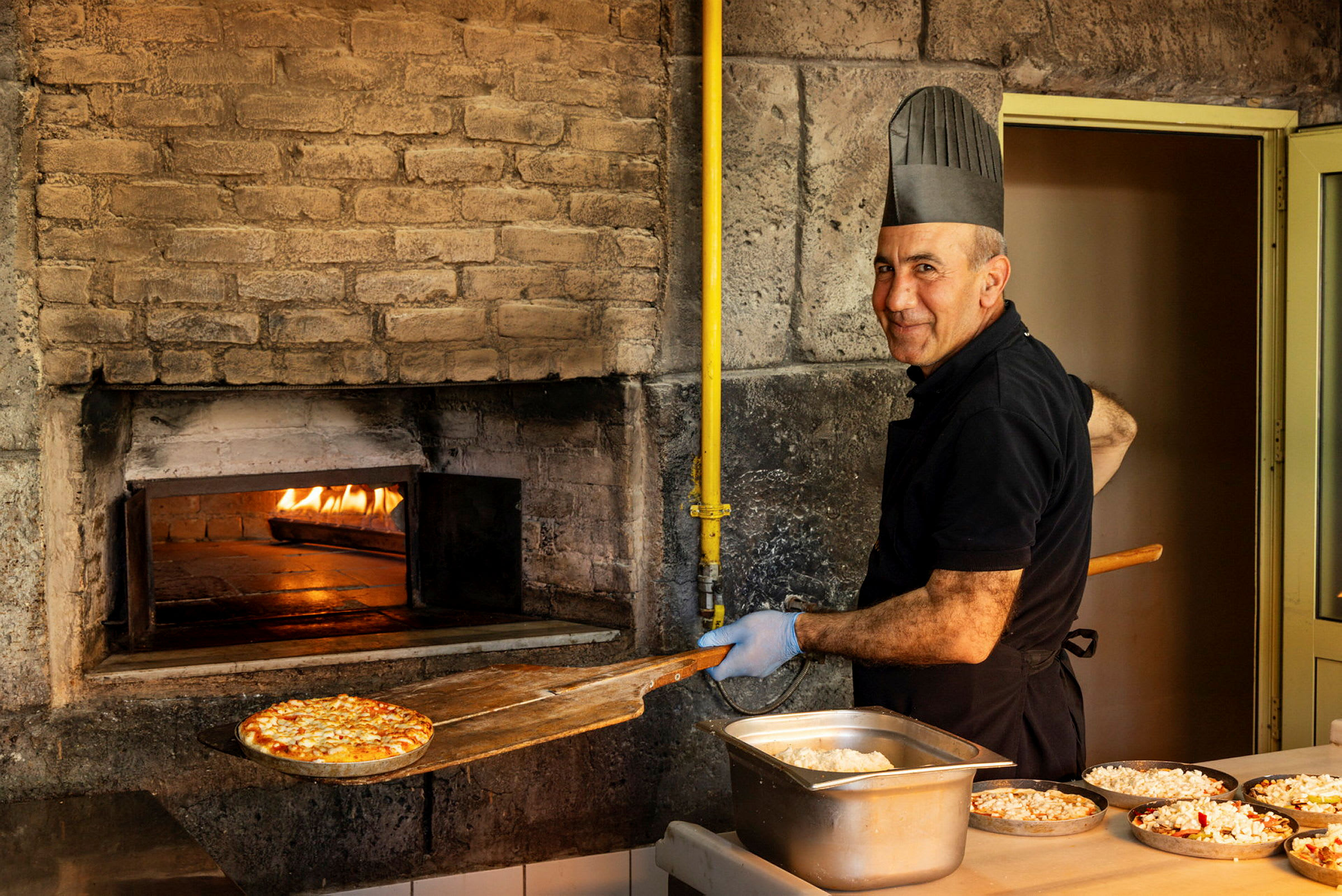 En pizzabagare som tar ut en pizza ur en stenugn, redo att serveras. (AI-genererad text)
