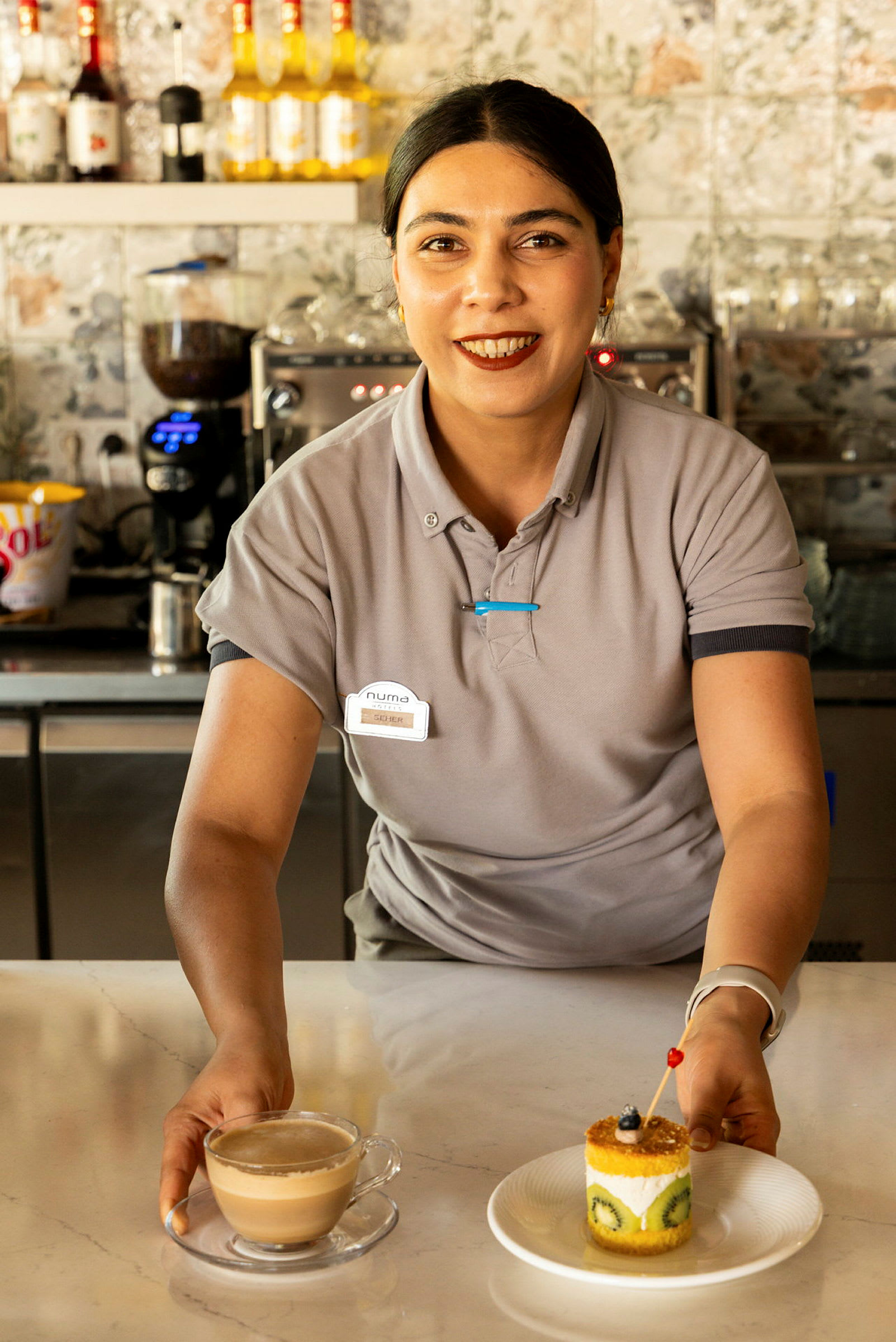 En person klädd i uniform håller i en kopp kaffe och en tallrik med en dessert bakelse på en disk. (AI-genererad text)
