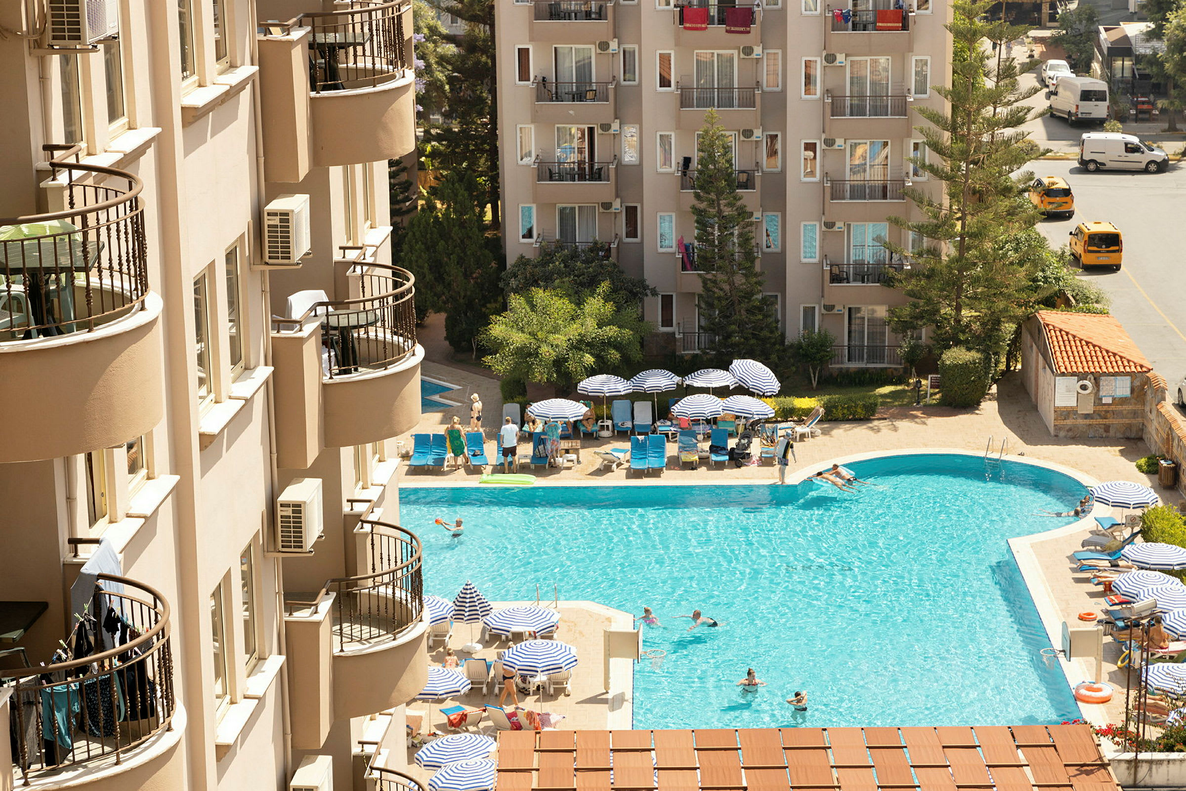 En hotellpool med solstolar och parasoller i närheten av byggnader. (AI-genererad text)