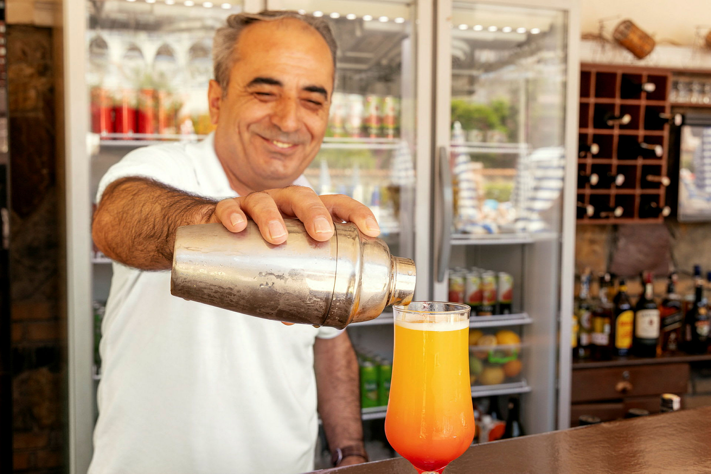 En person håller en cocktailskakare och häller en dryck i ett glas. (AI-genererad text)