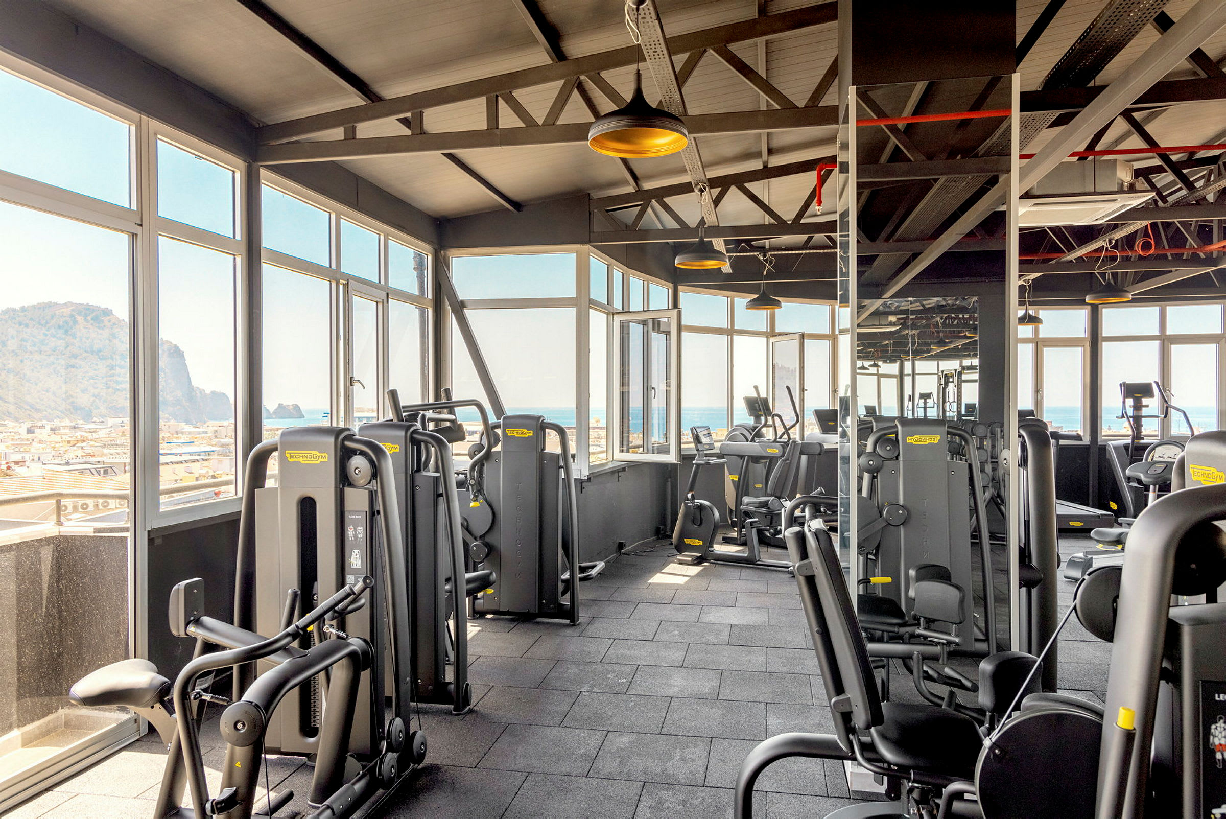Ett gym med träningsmaskiner och stora fönster som visar utsikt över havet. (AI-genererad text)