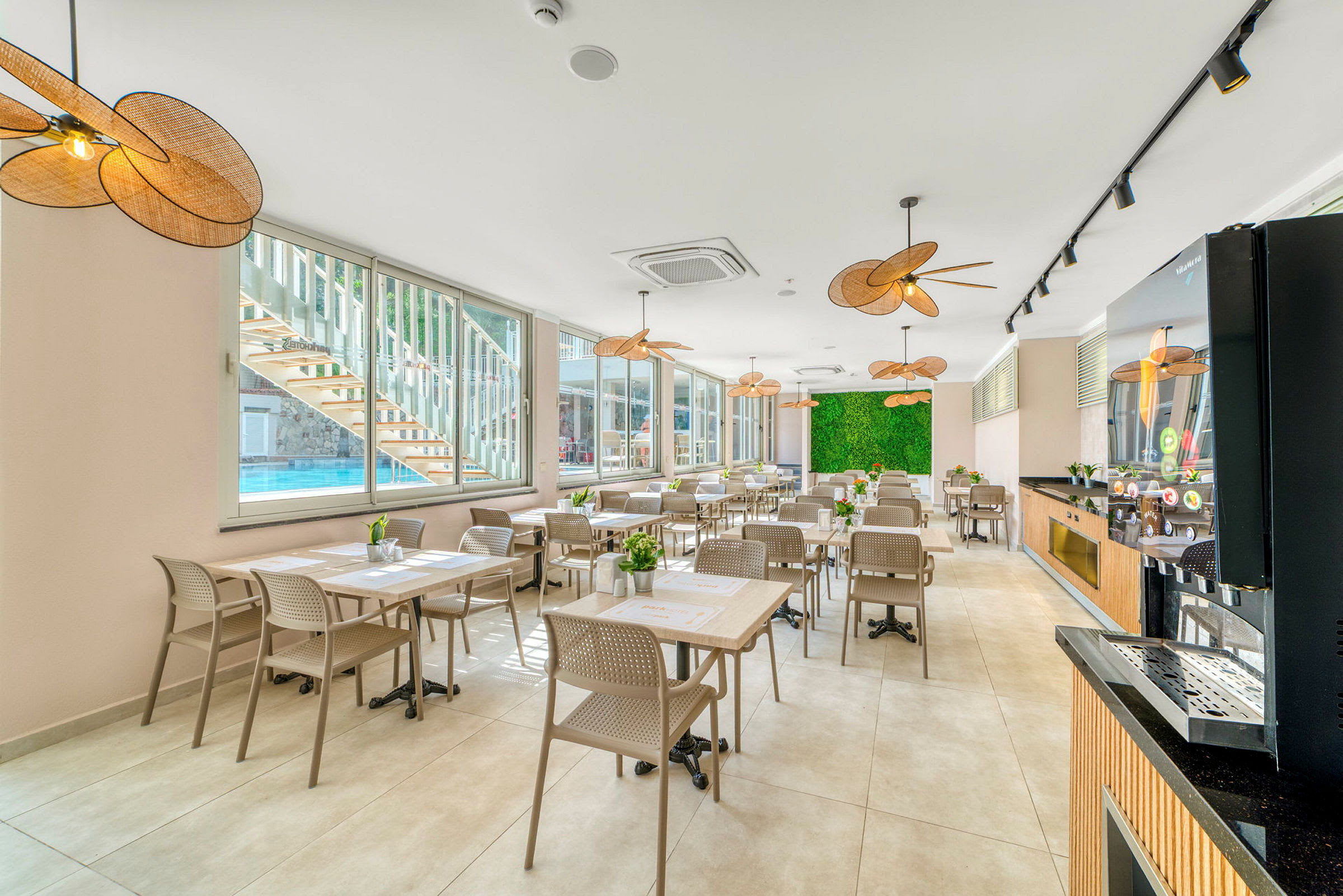Restaurang med bord och stolar, stora fönster och grön dekorativ vägg. (AI-genererad text)